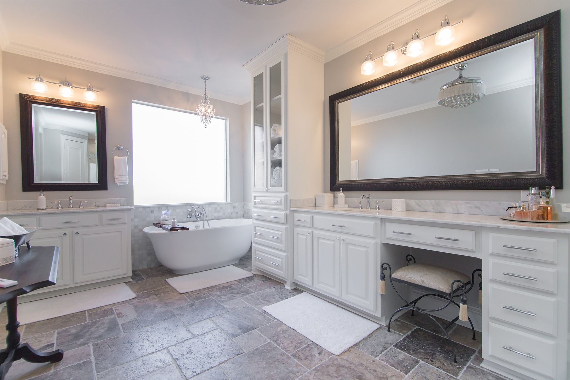 Spacious white bathroom with tub, vanity, cabinets, and large mirrors. Gray stone flooring. - After