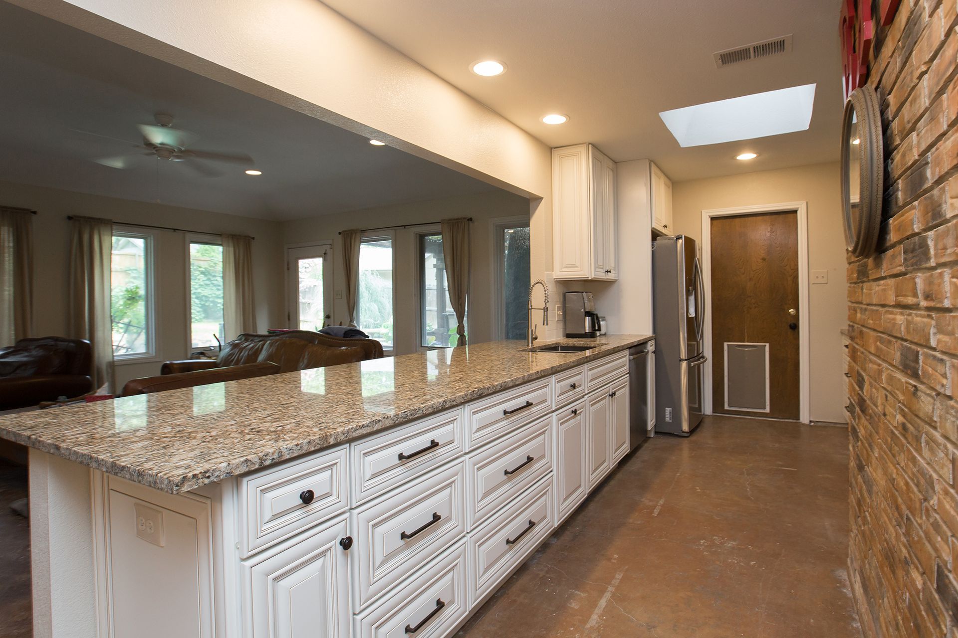 Kitchen with white cabinets, granite countertop, brick wall, and view into living room. - After