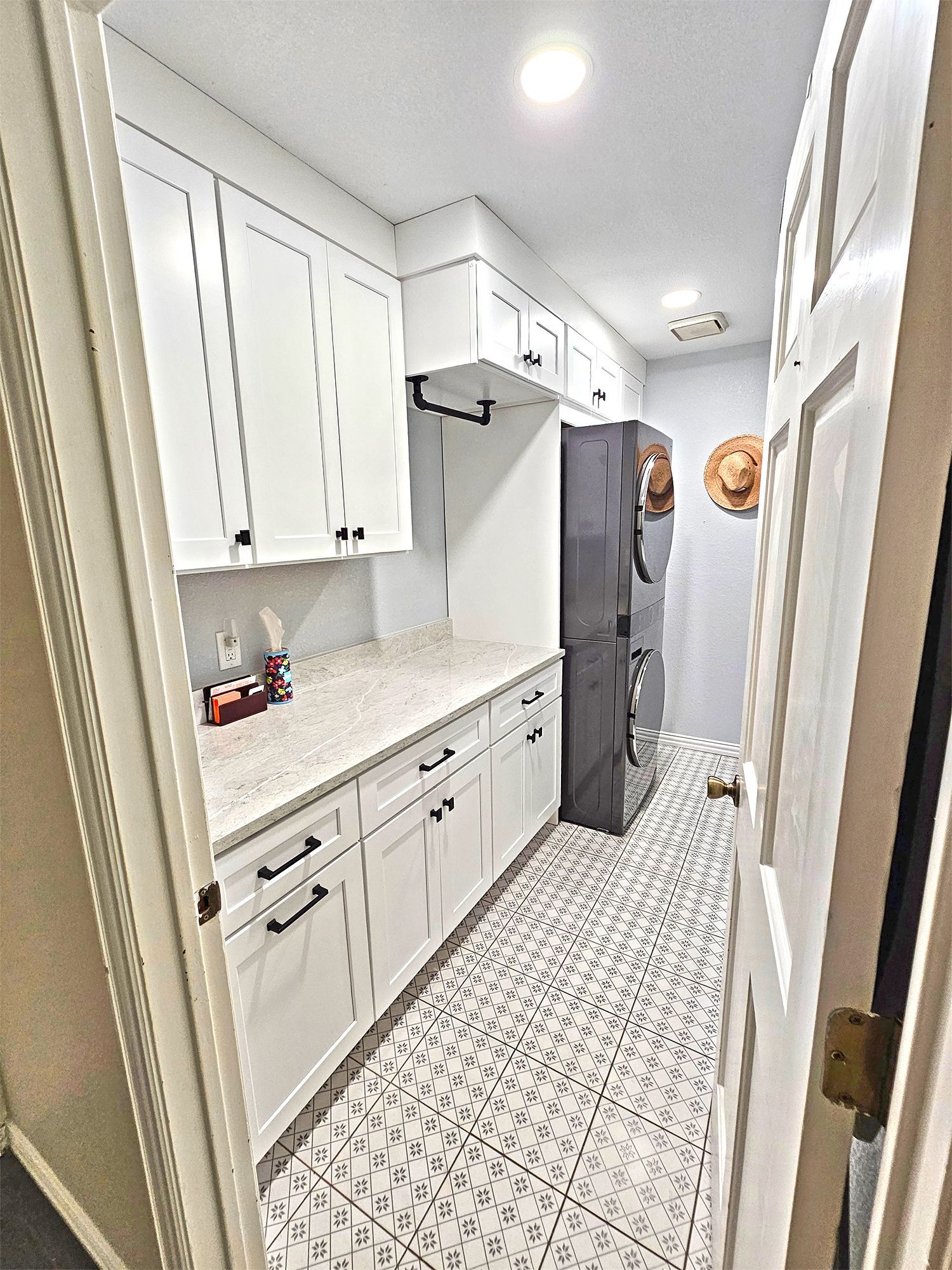 Narrow, white pantry with white cabinets, countertop, and patterned floor. Dark refrigerator. - After