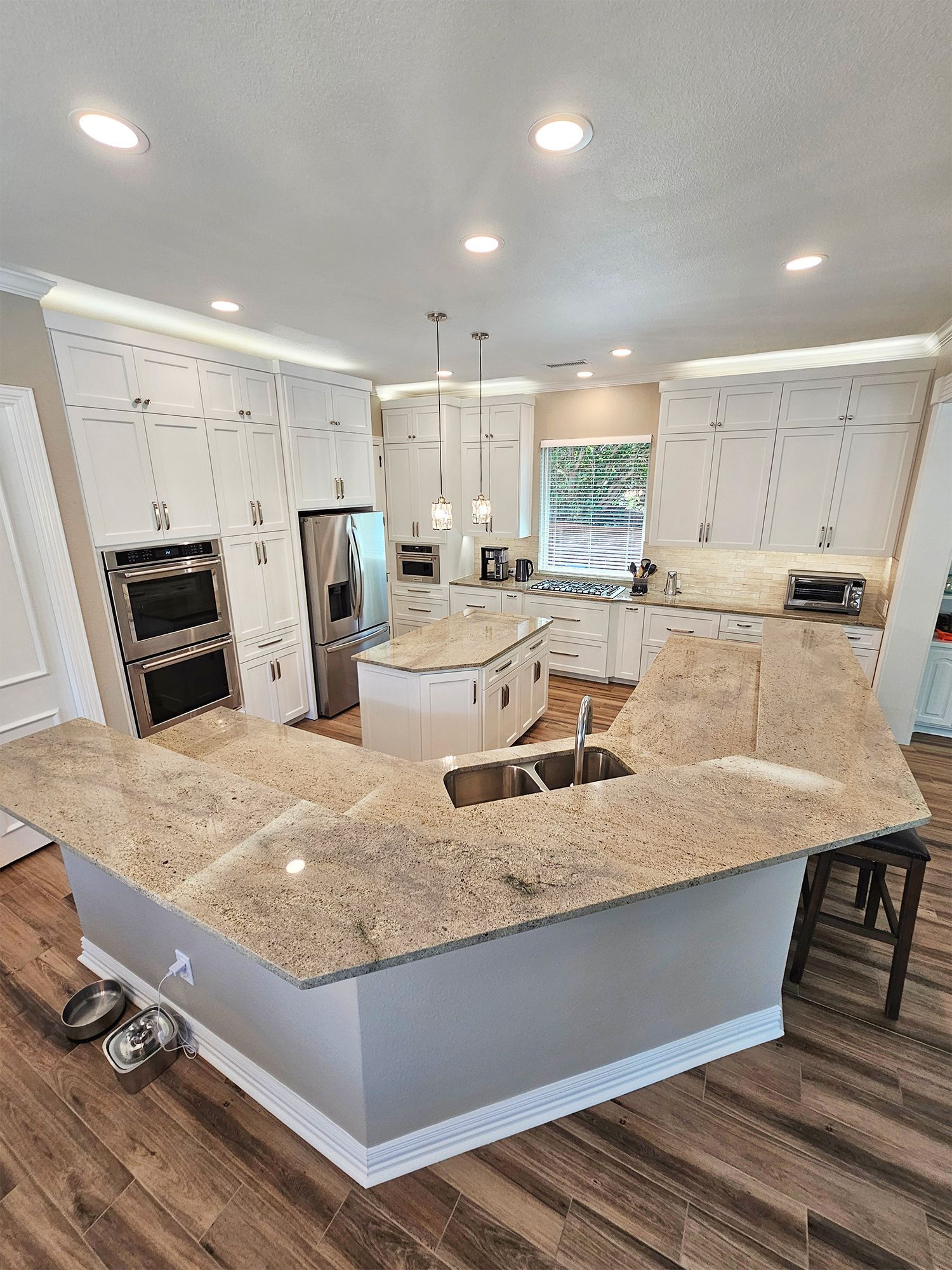 Modern kitchen with light granite countertops, white cabinets, and hardwood floors. - After