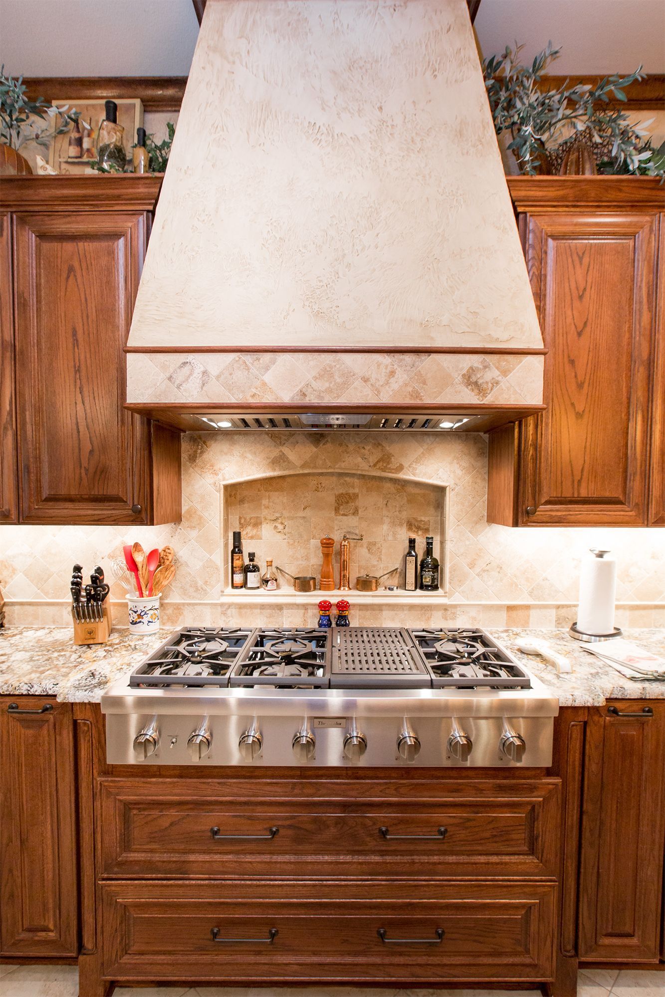 A stainless steel range sits beneath a tan-colored hood in a wood-paneled kitchen. - After