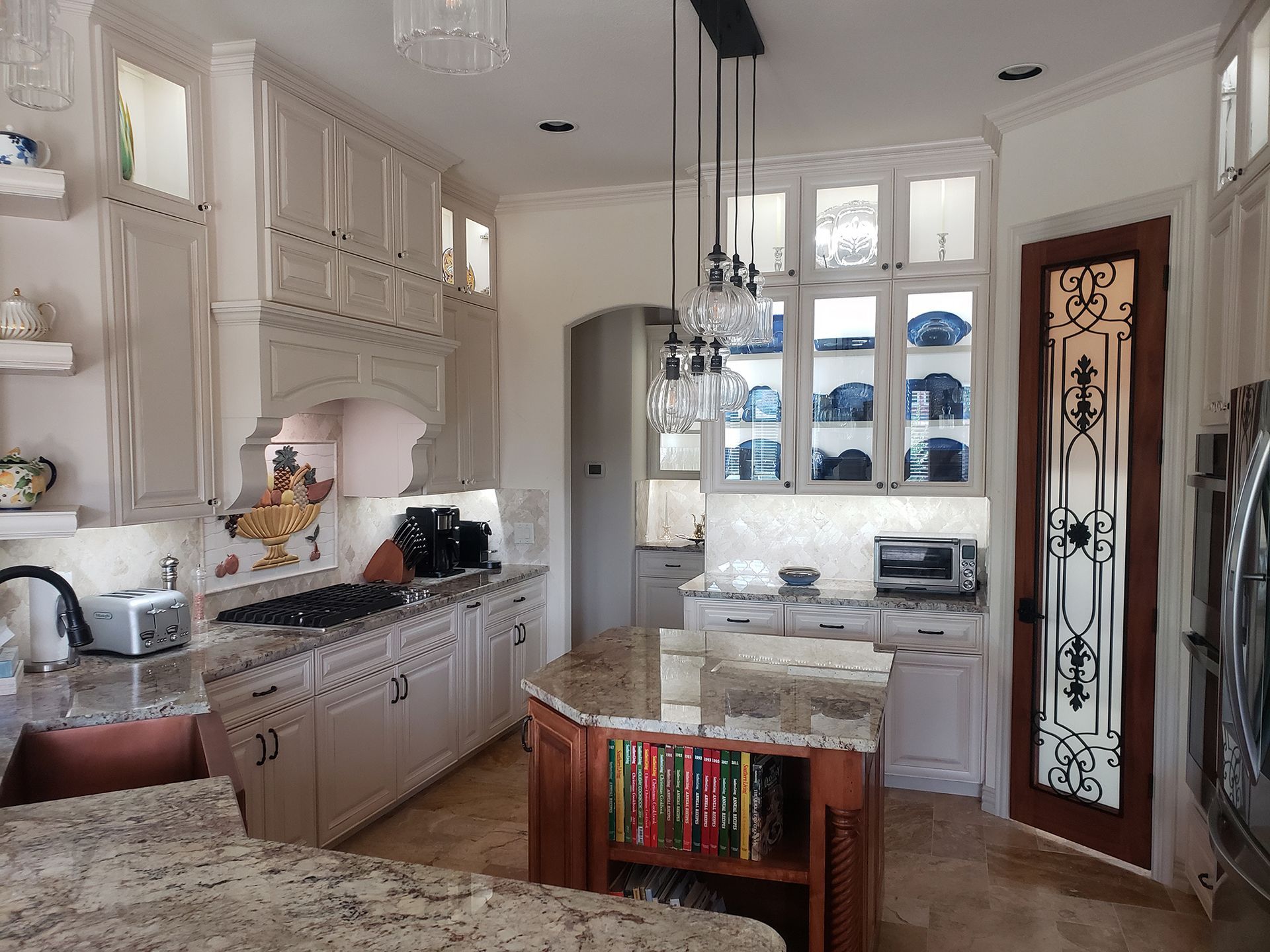 Elegant white kitchen with granite countertops, glass-front cabinets, island, and pendant lights. - After