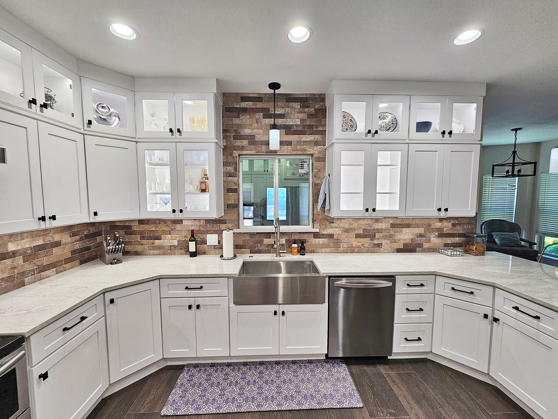 White kitchen cabinets with a stainless steel sink and brick backsplash. - After