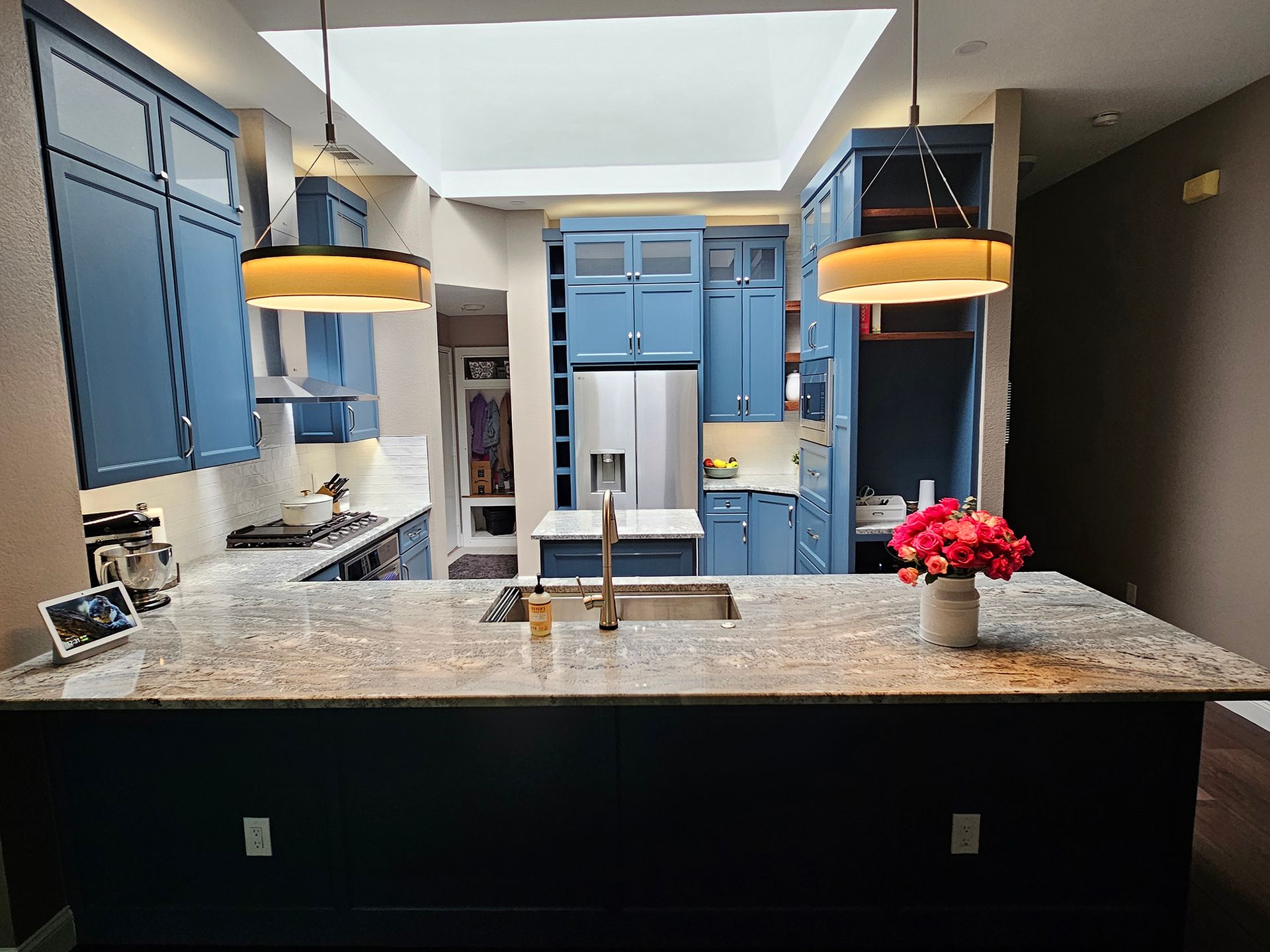 Blue kitchen with granite countertops, island, and pendant lights; bright skylight. - After