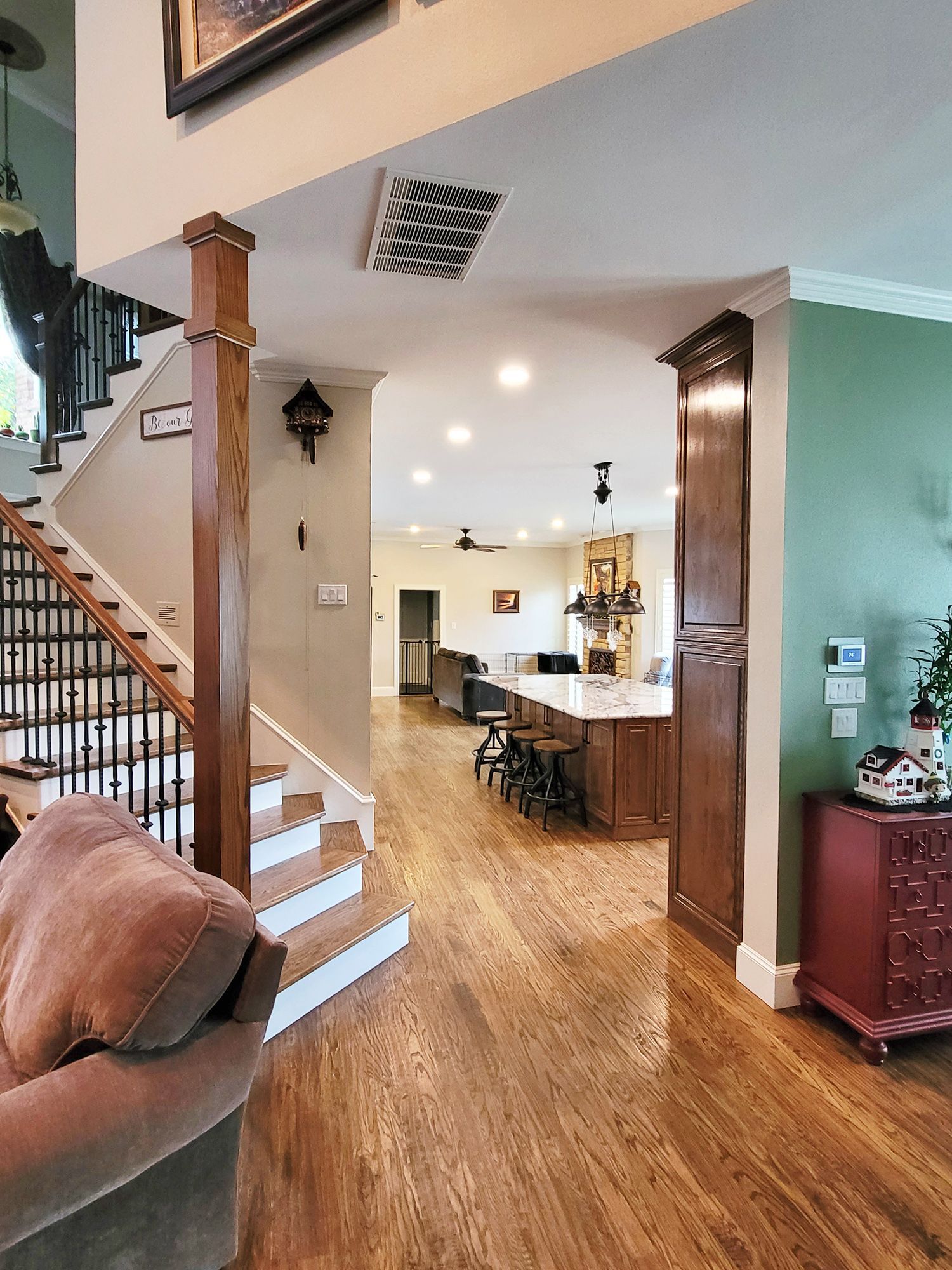 Interior view of a home with wooden floors, stairs, and a kitchen island with stools. - After