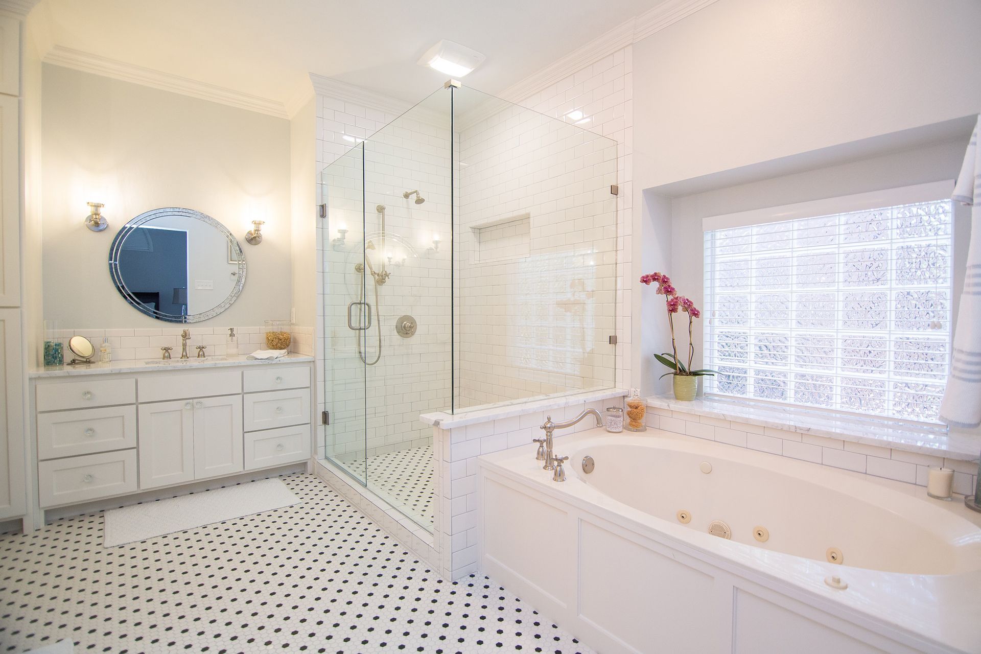 Spacious, bright white bathroom with shower, tub, vanity, and glass block window; black and white tiled floor. - After