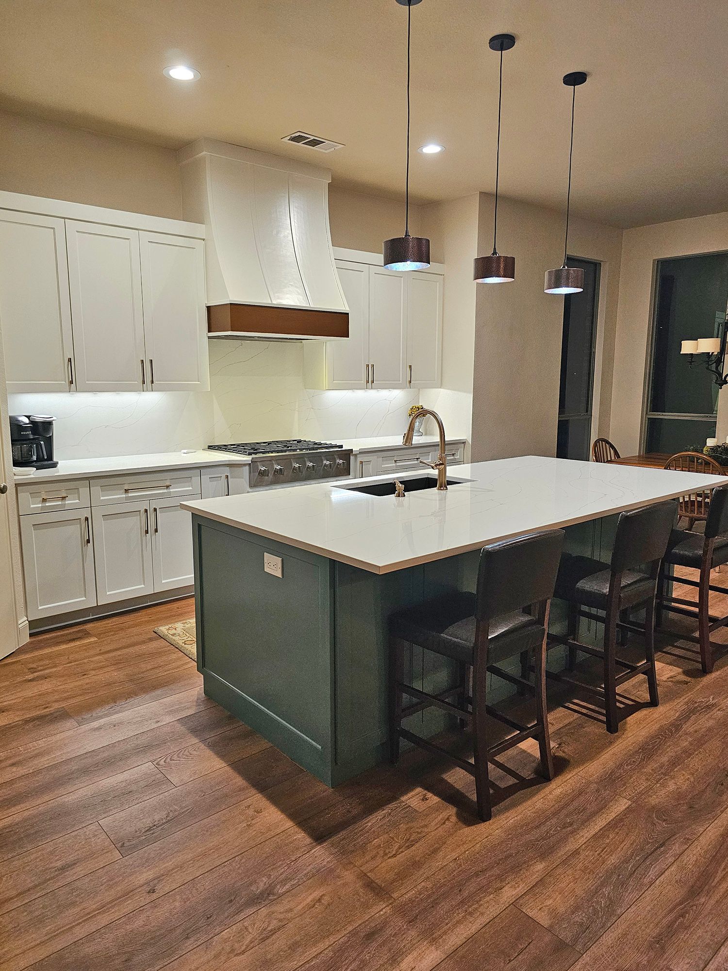 Modern kitchen with white cabinets, a green island, and dark pendant lights. - After