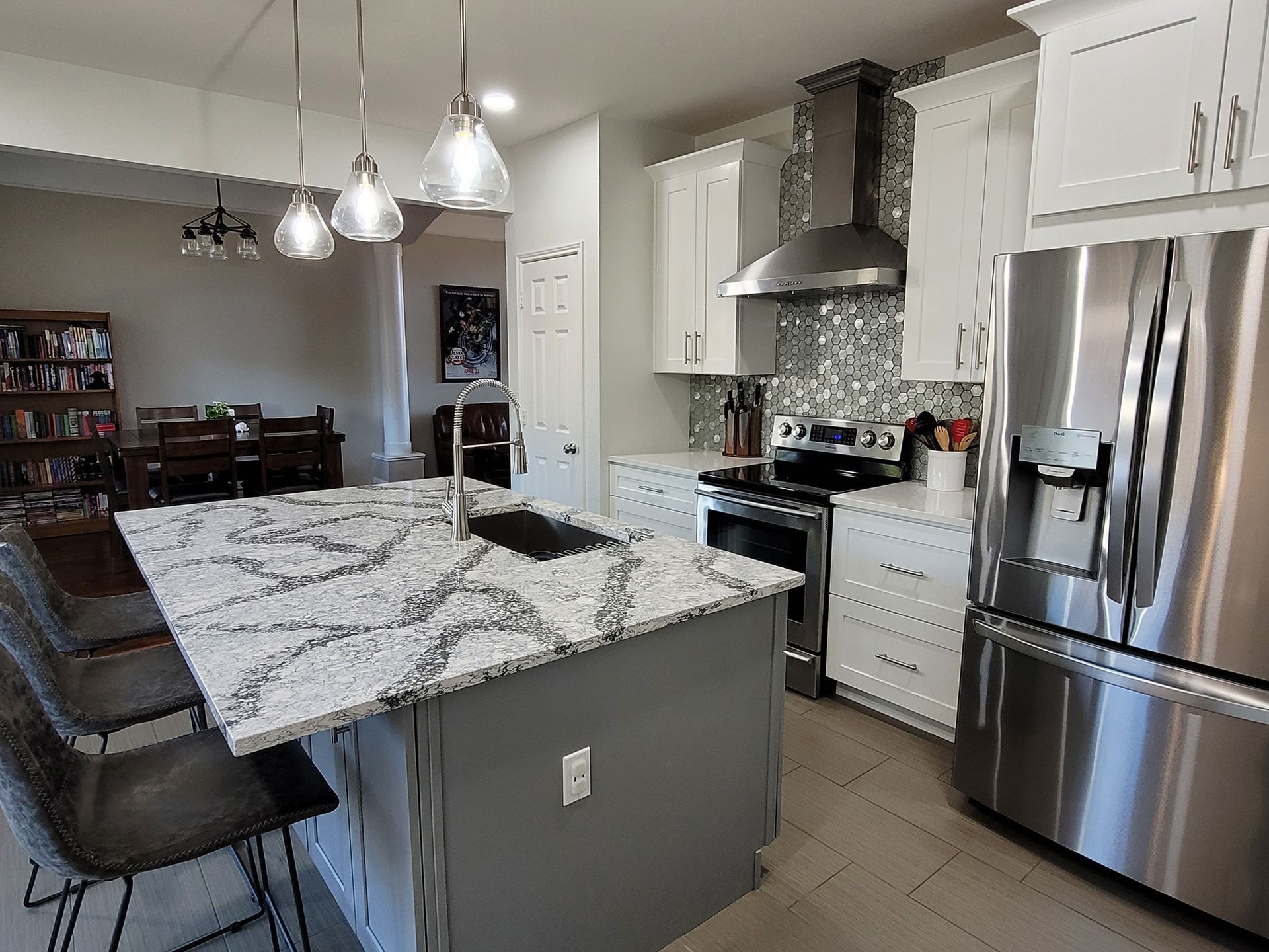 Modern kitchen with gray island, white cabinets, stainless steel appliances, and a stone countertop. - After