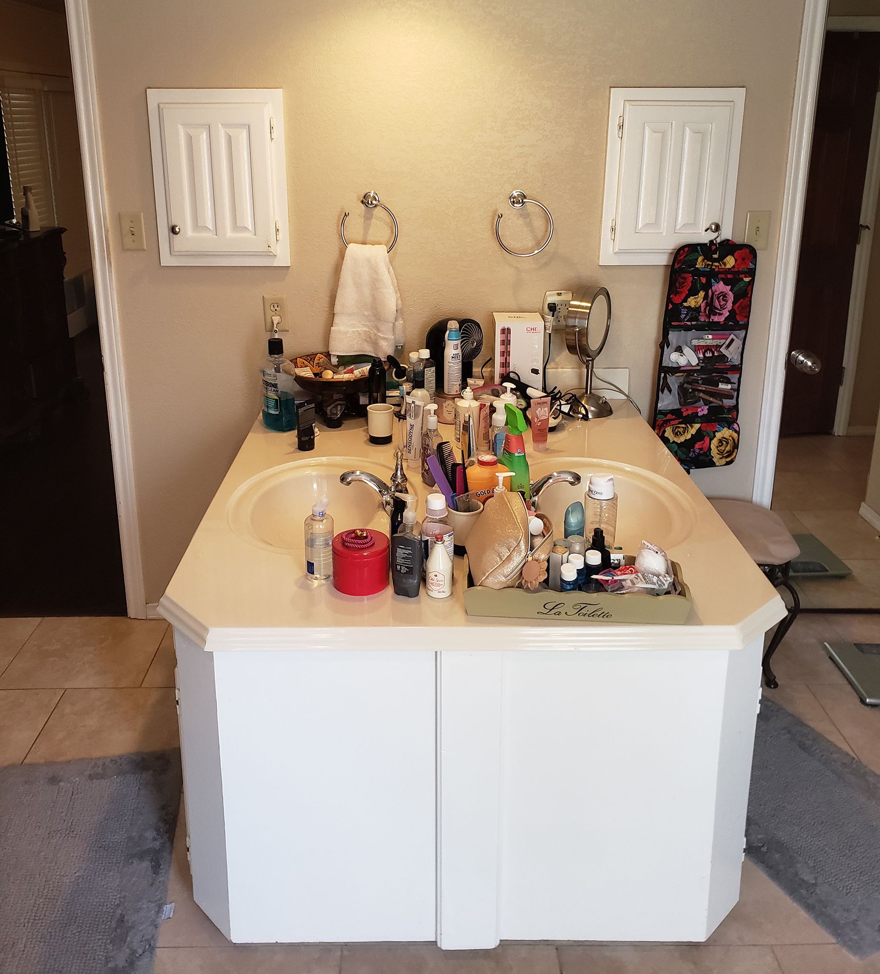 Double white bathroom vanity with cluttered counter, two mirrors, and two wall cabinets. - Before