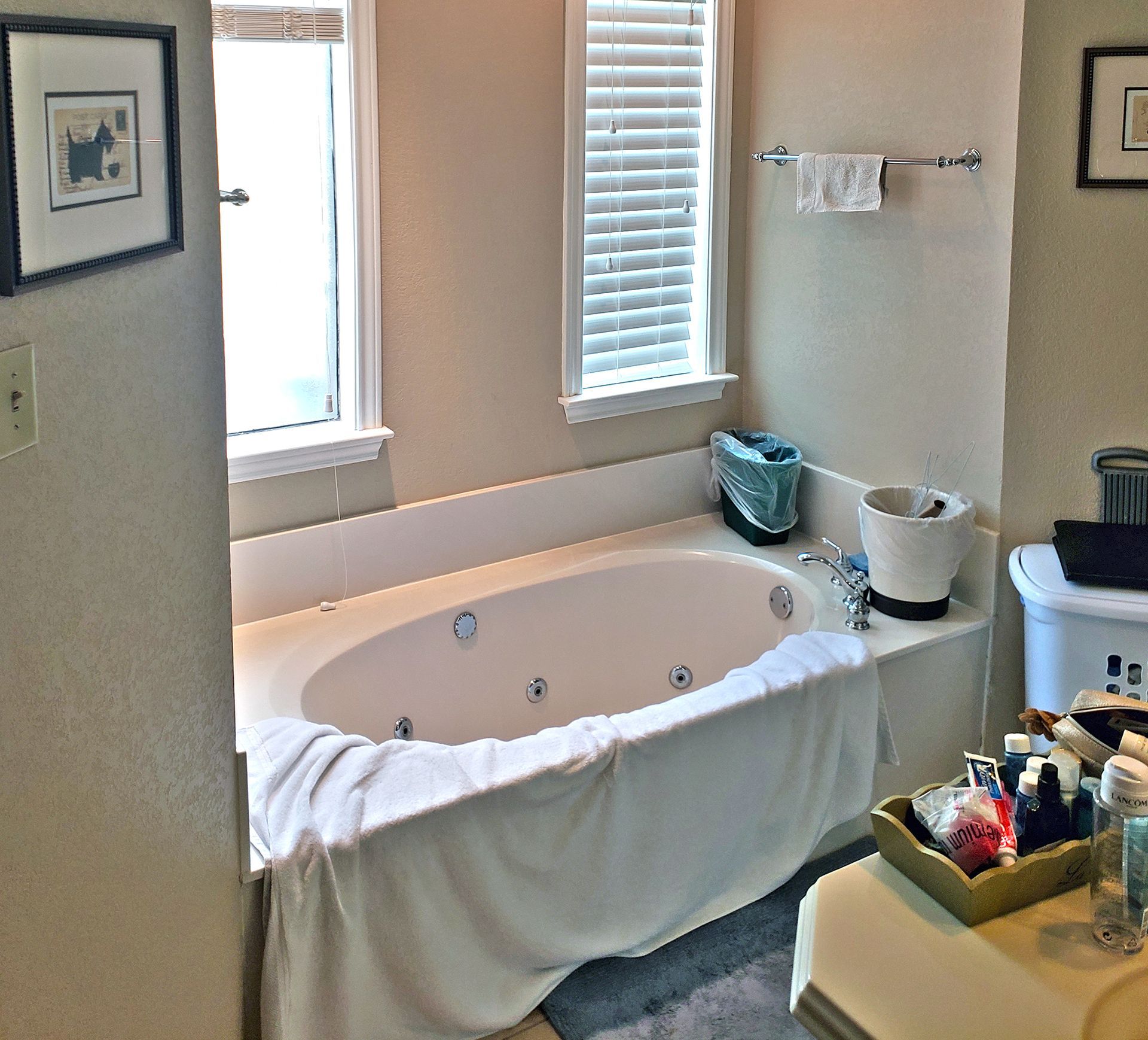 Bathroom with oval tub, windows, and toiletries on a counter. - Before