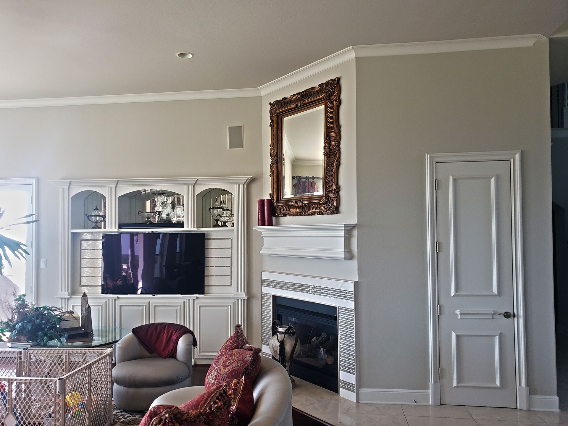 Living room with fireplace, mirror, built-in entertainment center, two armchairs, and a door. - Before