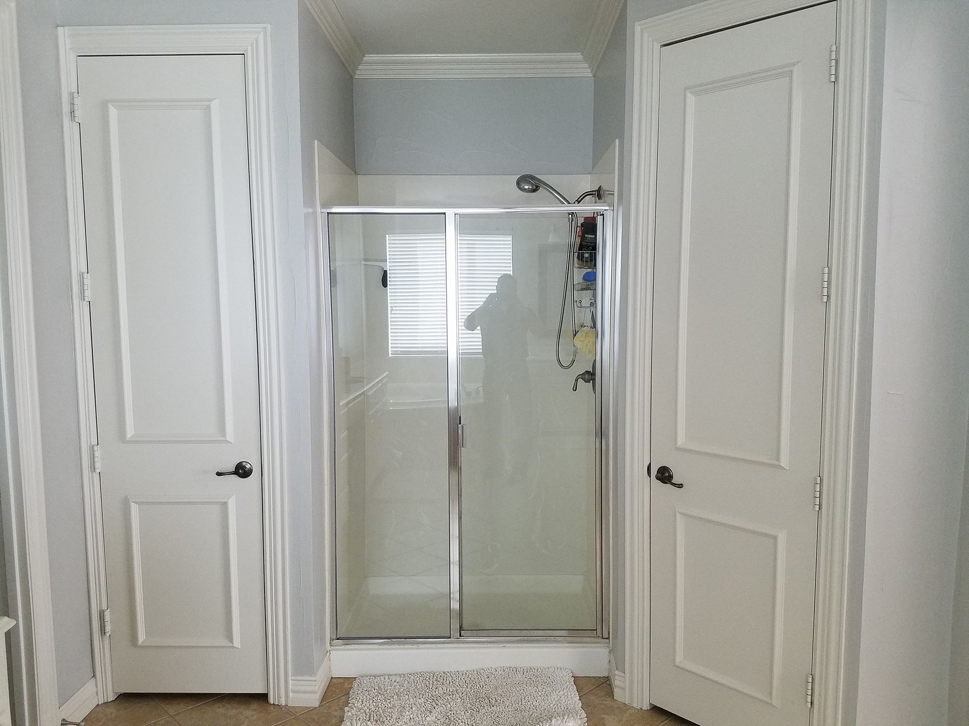 A bathroom with a glass shower, two white doors, and a rug. - Before