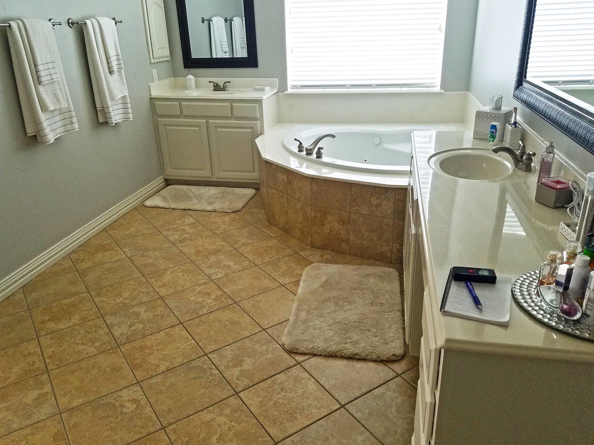 Bathroom with beige tile floor, vanity, tub, and towels. - Before