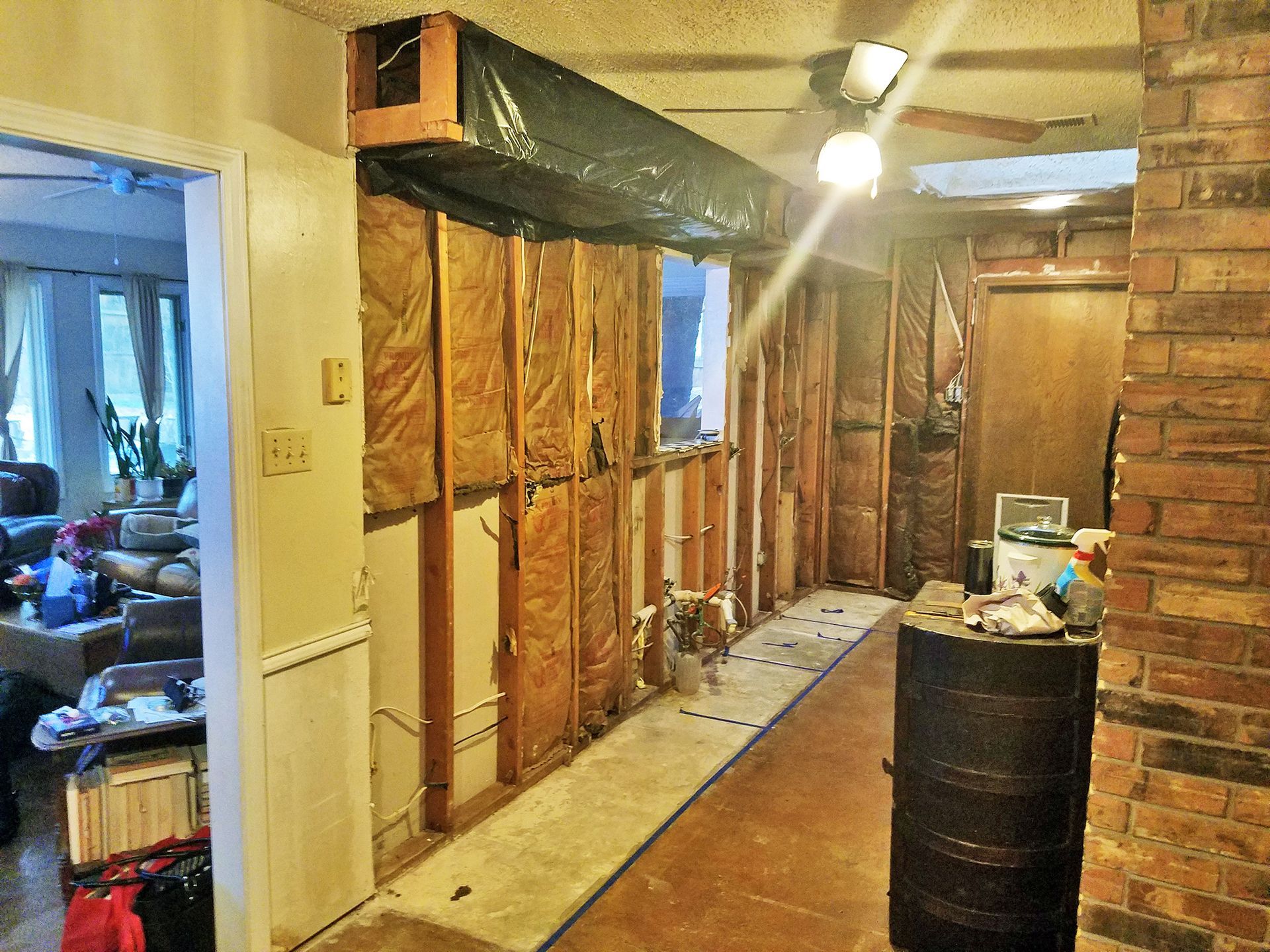 Interior wall under construction; exposed framing and insulation. A black duct and exposed brick column. - Before