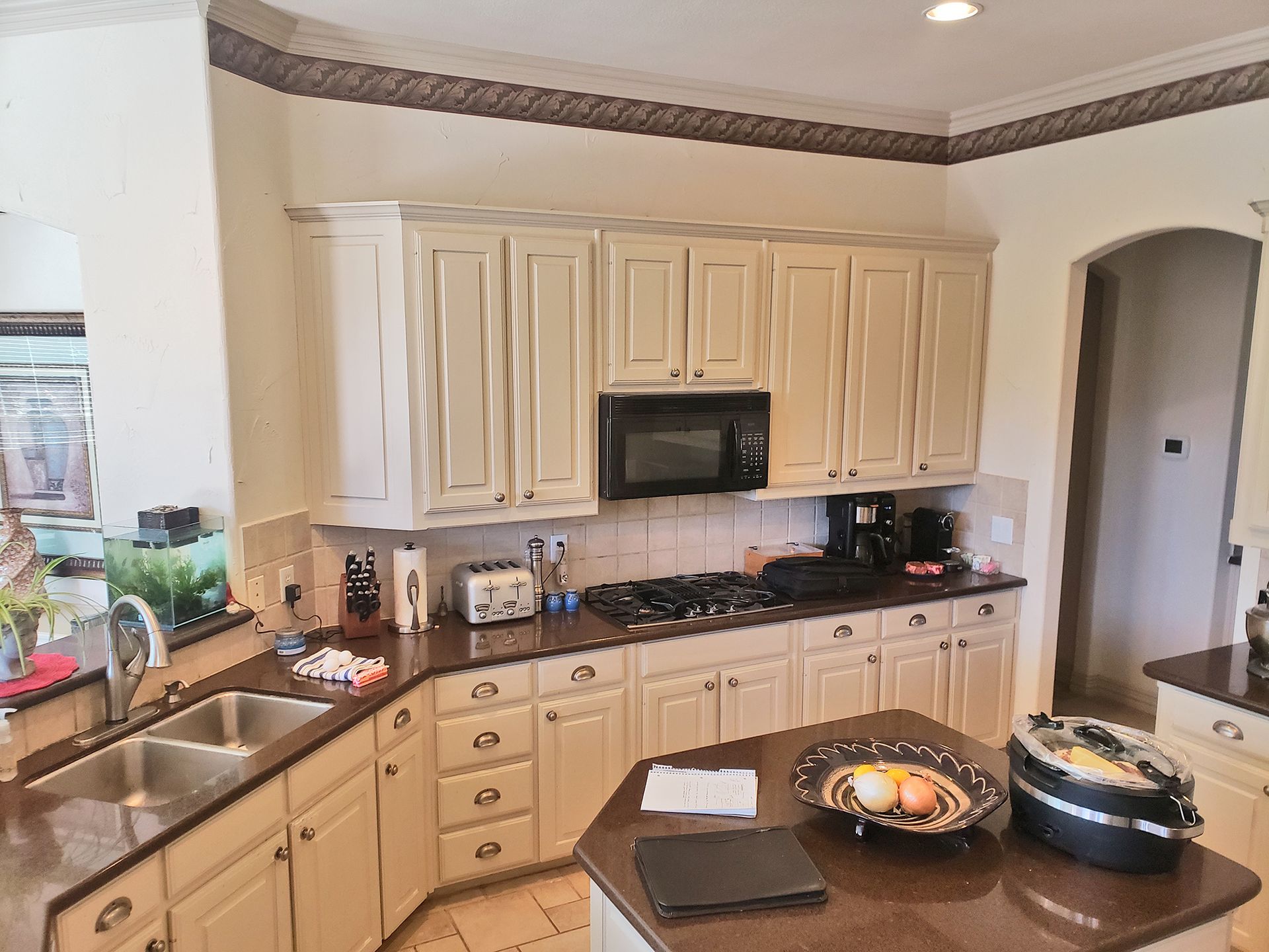 Cream-colored kitchen with cabinets, appliances, and an island. A sink is on the left. - Before