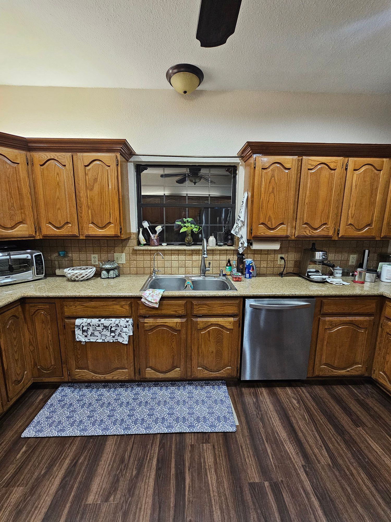 Kitchen with wooden cabinets, stainless steel appliances, and a window above the sink. - Before