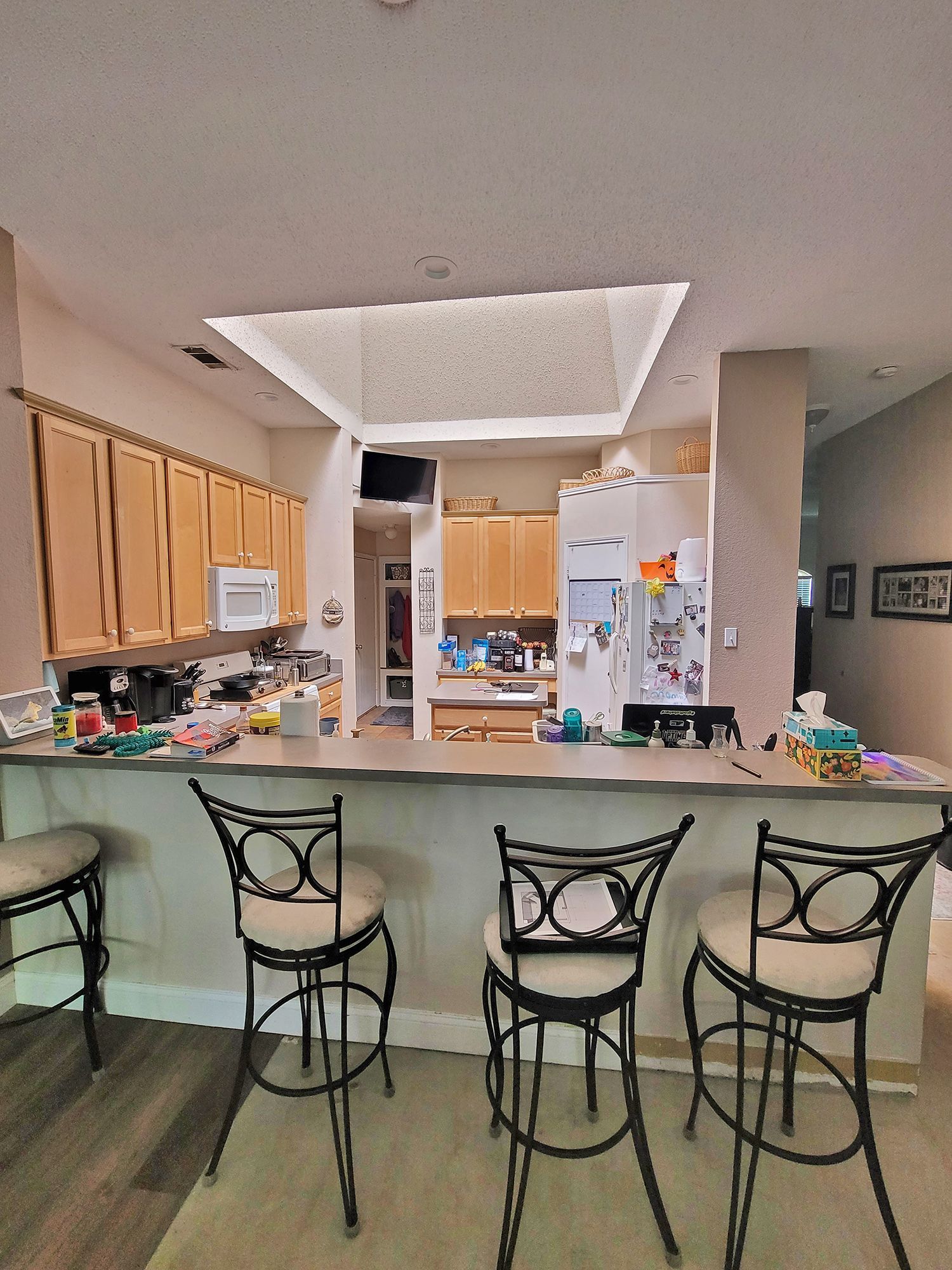 A kitchen with a counter and bar stools. Wooden cabinets and a refrigerator are visible. - Before
