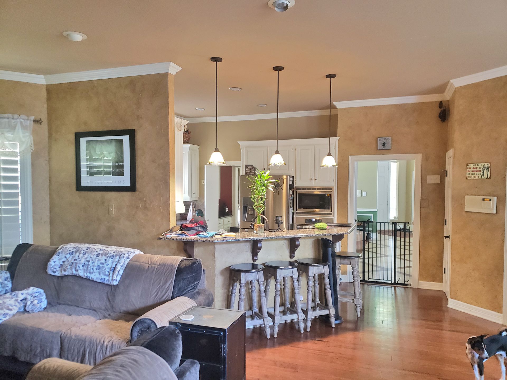 Living room with kitchen island, brown couch, pendant lights, and white cabinets. - Before