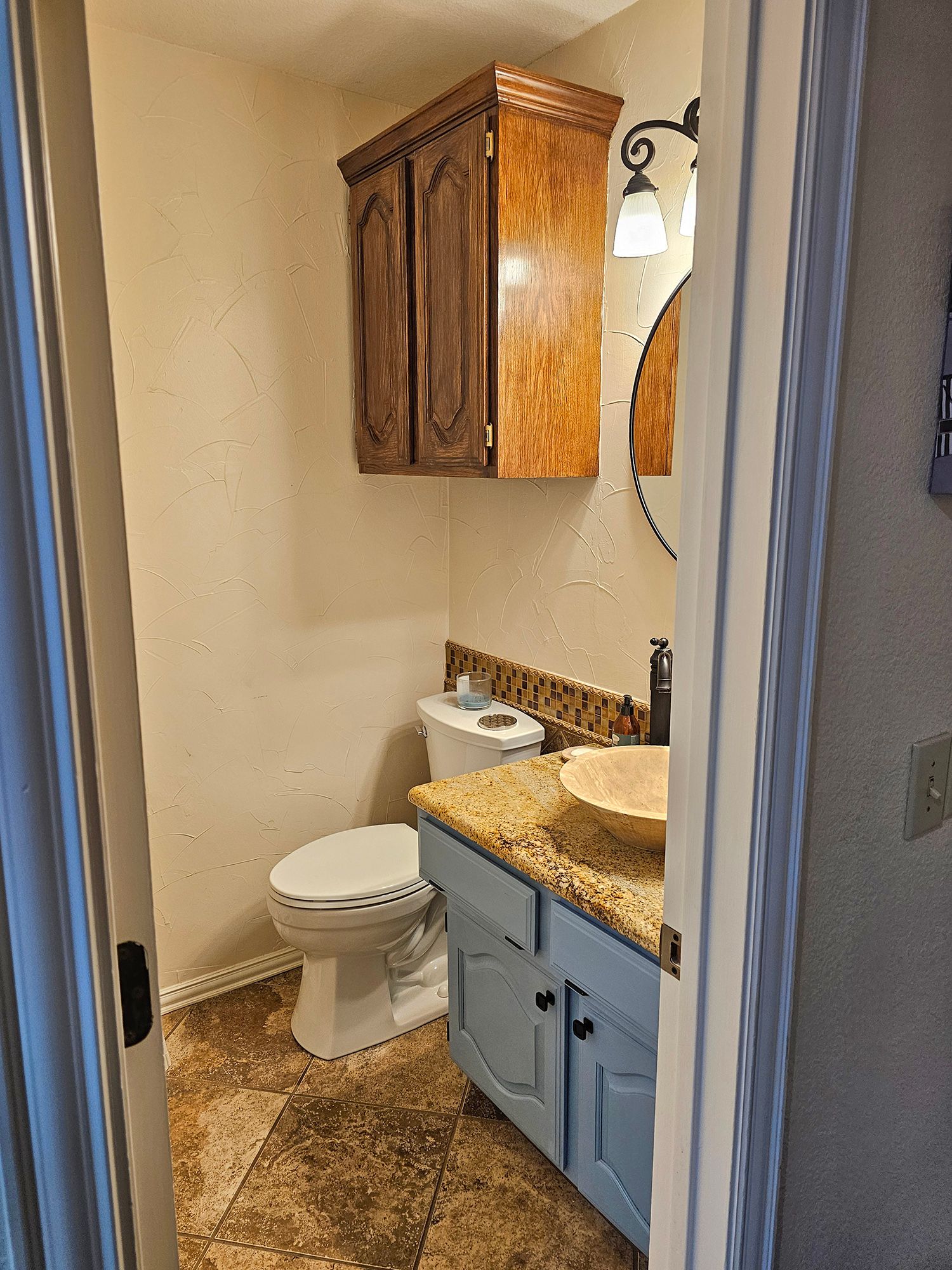 Small bathroom with a blue vanity, toilet, and wood-toned cabinet. - Before