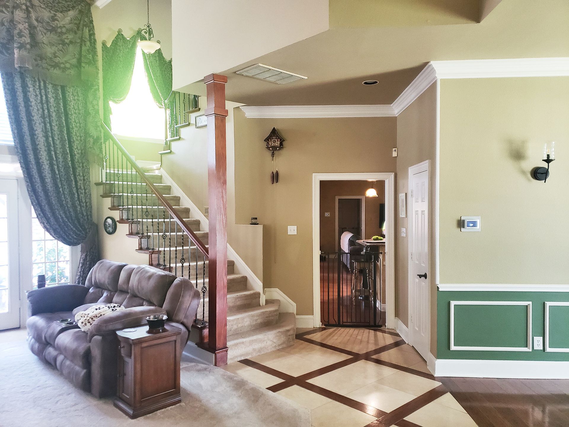 Living room with staircase, sofa, and door to another room; green and brown accents. - Before