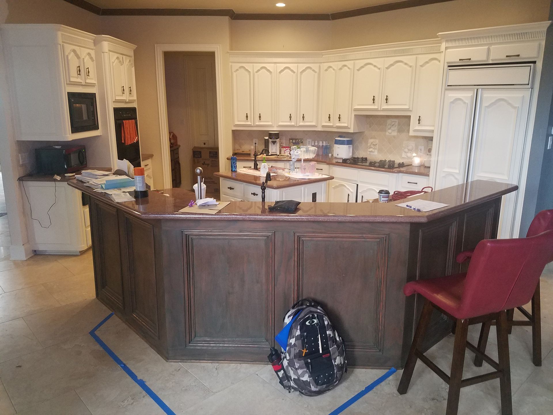A kitchen with brown island and white cabinets. A backpack sits near the island. - Before