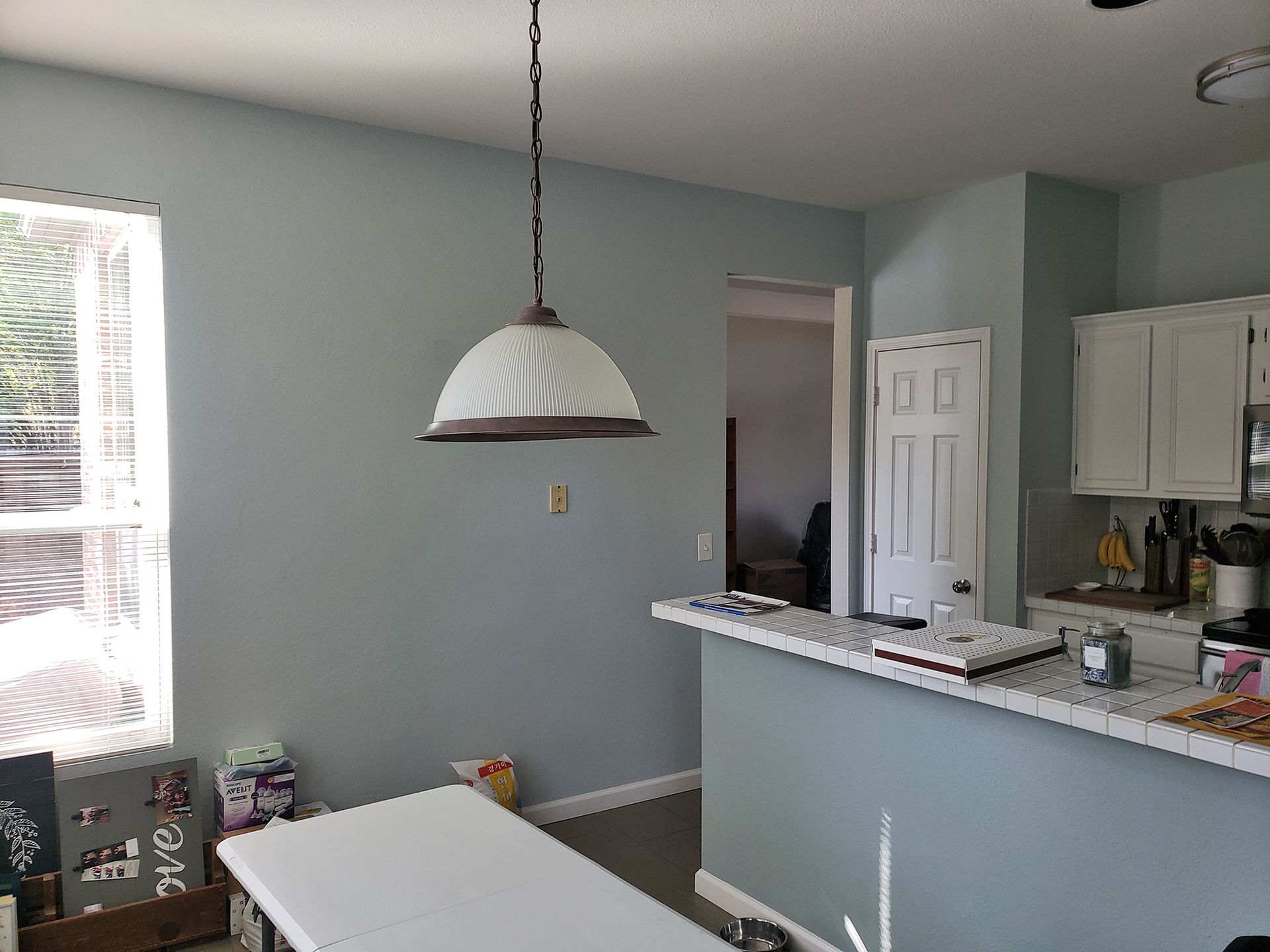 Kitchen with blue walls, white cabinets, a pendant light, and a breakfast bar. - Before