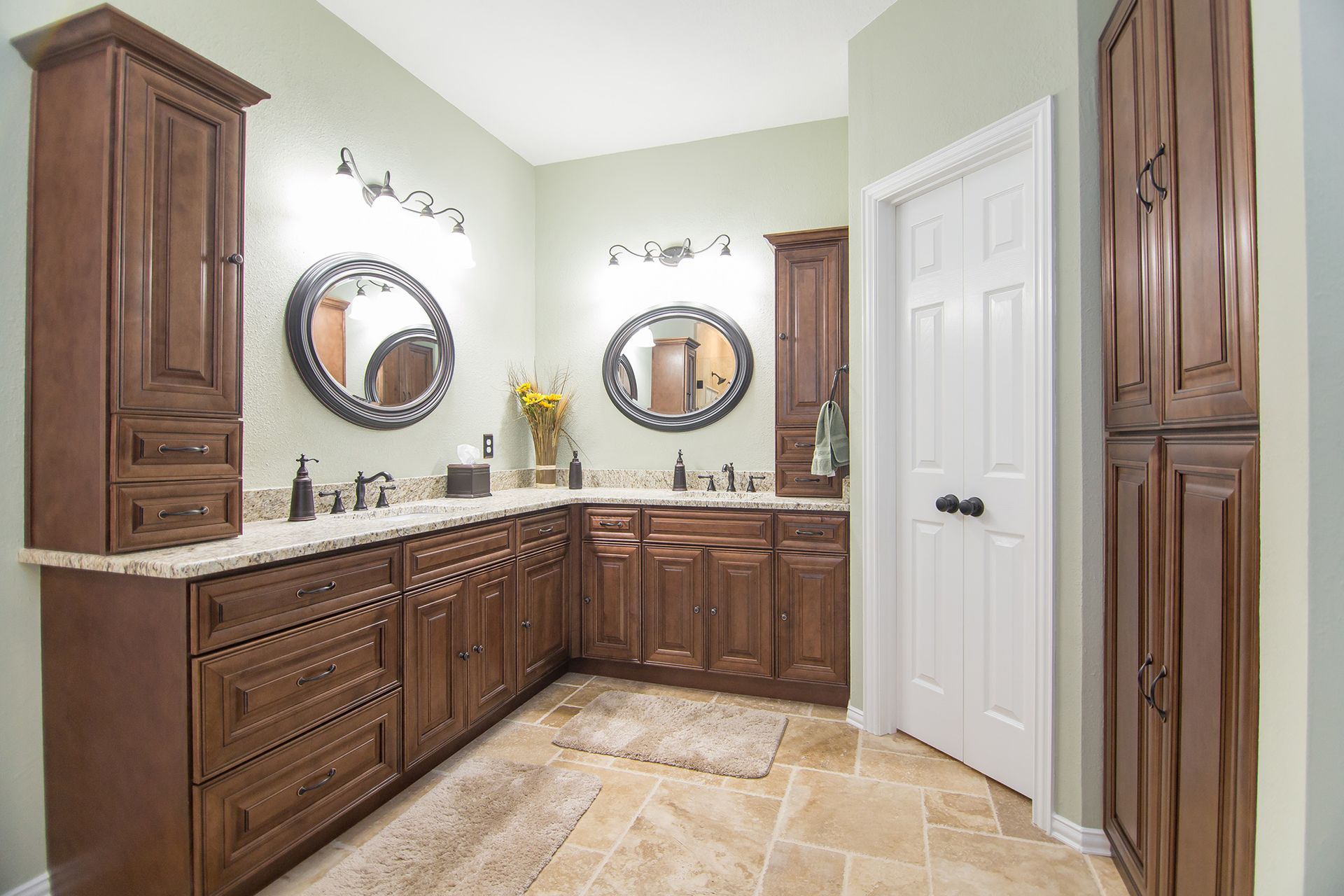 Bathroom with brown cabinets, light countertops, and round mirrors.