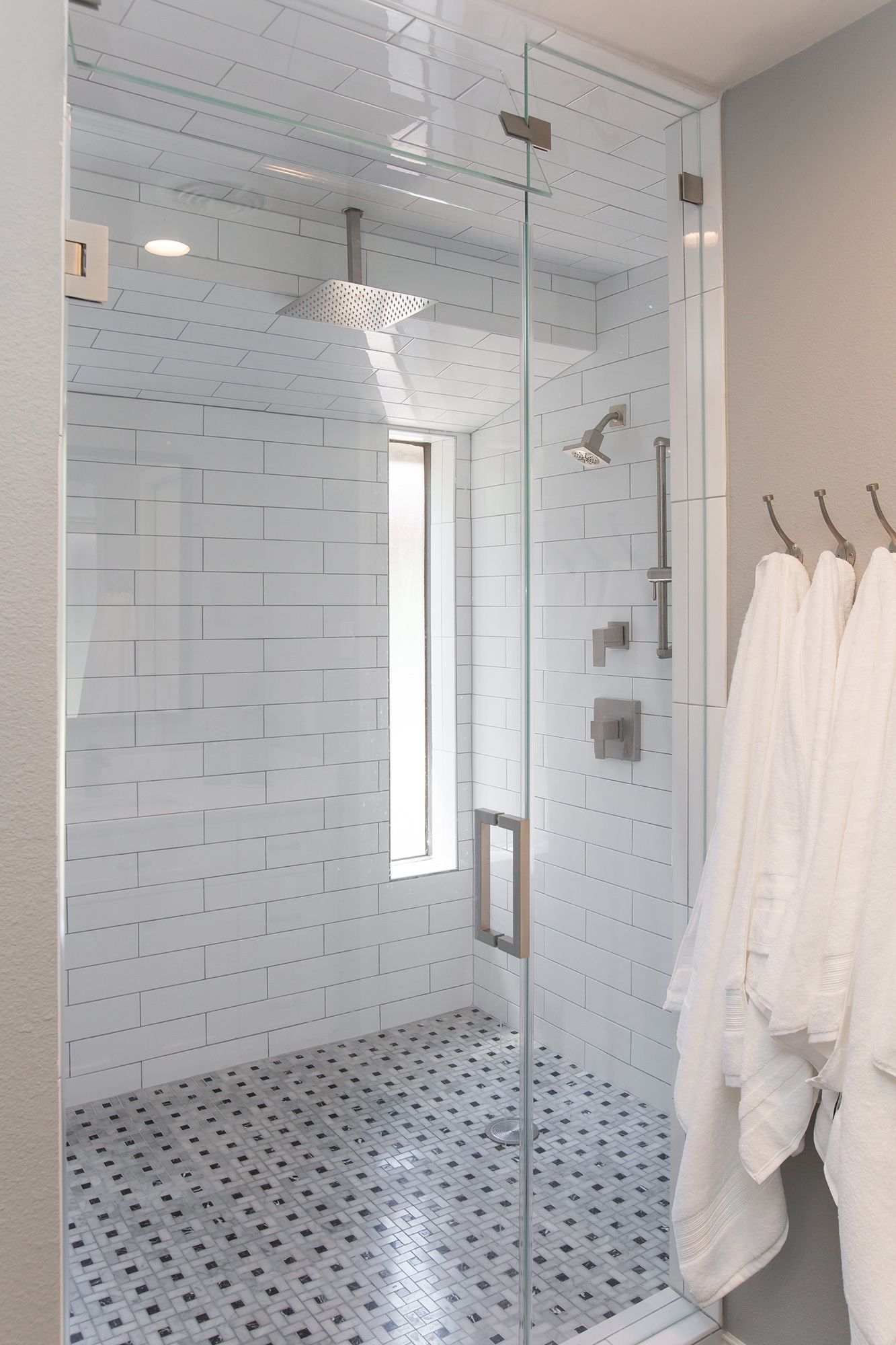 Modern bathroom with glass shower, white subway tiles, and robes hanging on the wall.
