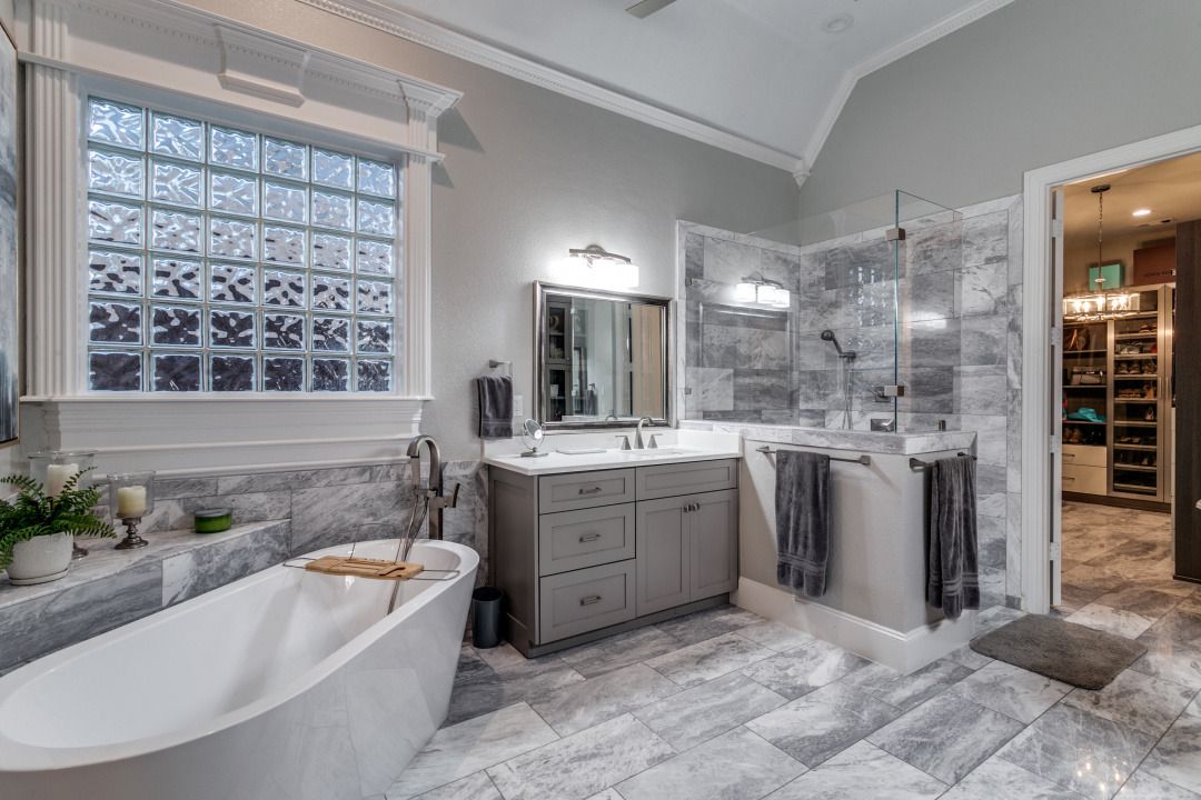 Luxurious bathroom with a freestanding tub, marble tile, and glass-block window.