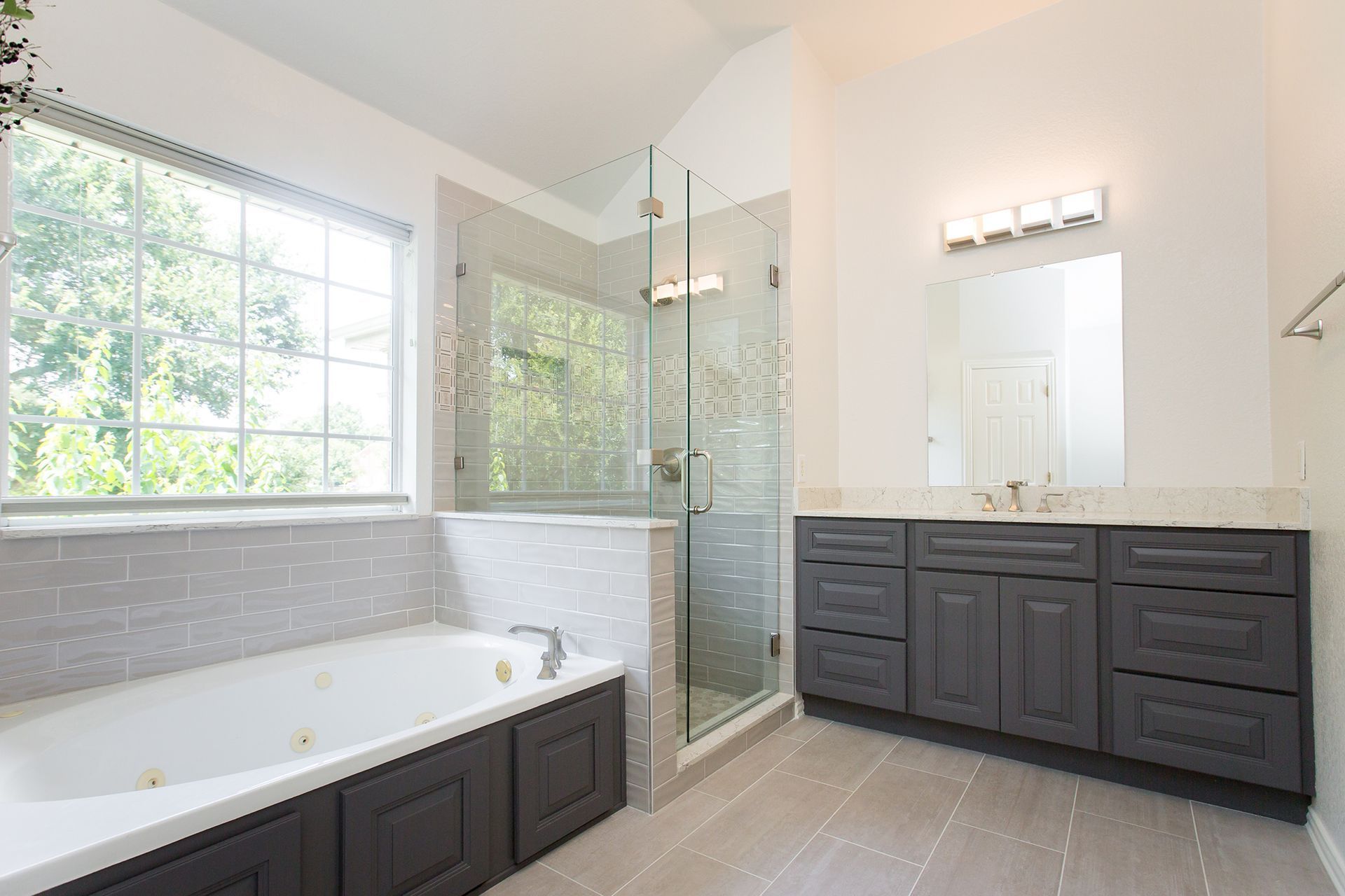 Spacious modern bathroom with a tub, glass shower, gray vanity, and large window.
