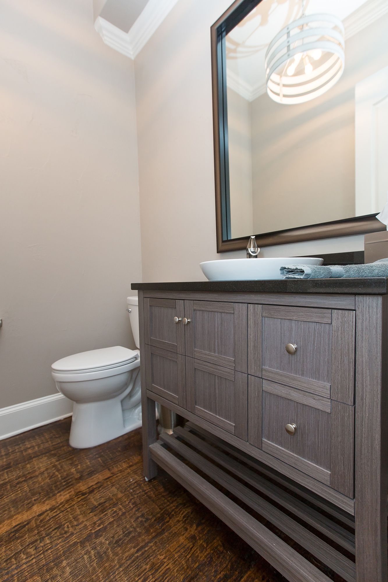Bathroom with gray vanity, white sink, and toilet; dark wood-look floor, neutral walls, and large mirror.