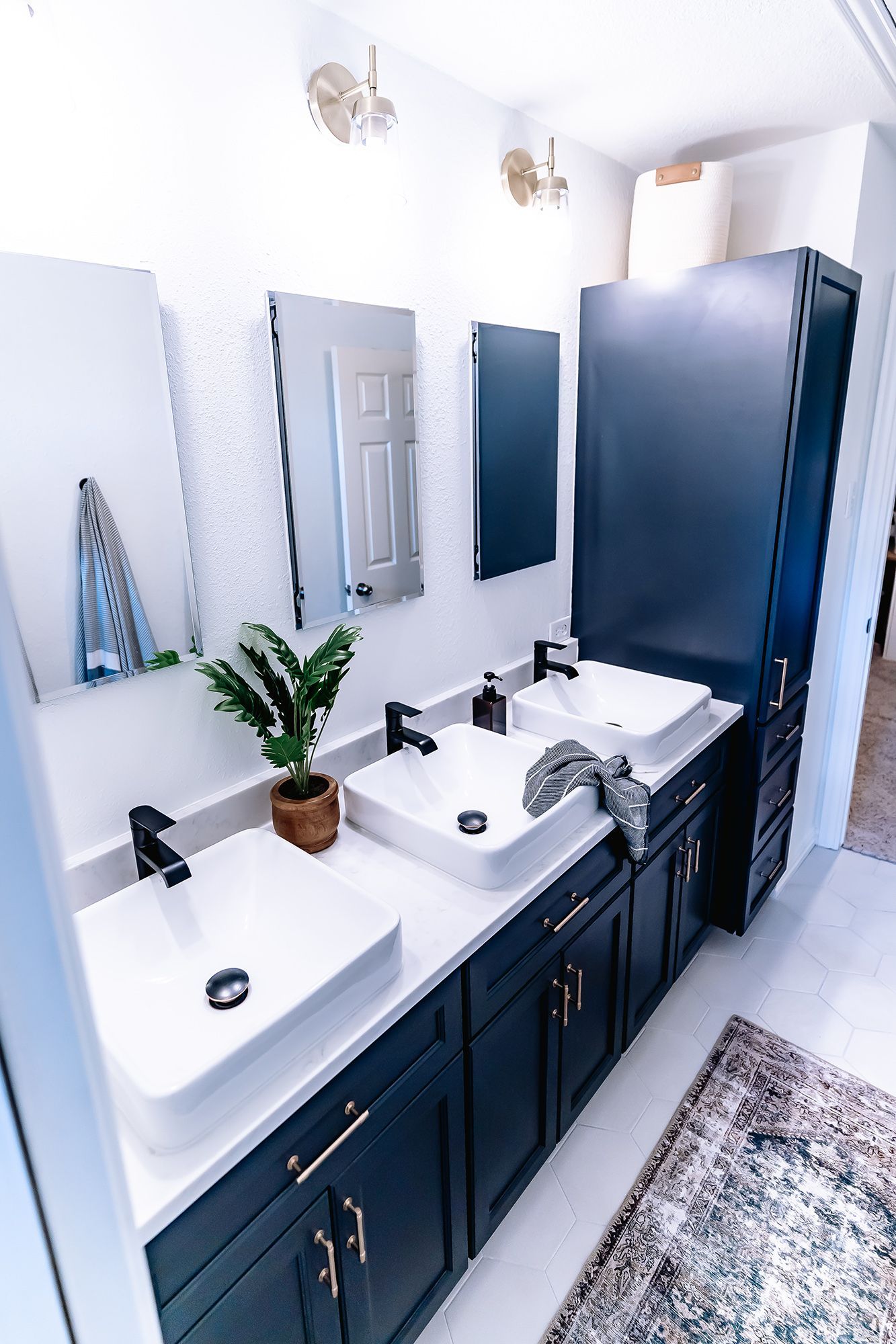 Bathroom with navy vanity, white sinks, black faucets, and gold hardware; rectangular mirrors.