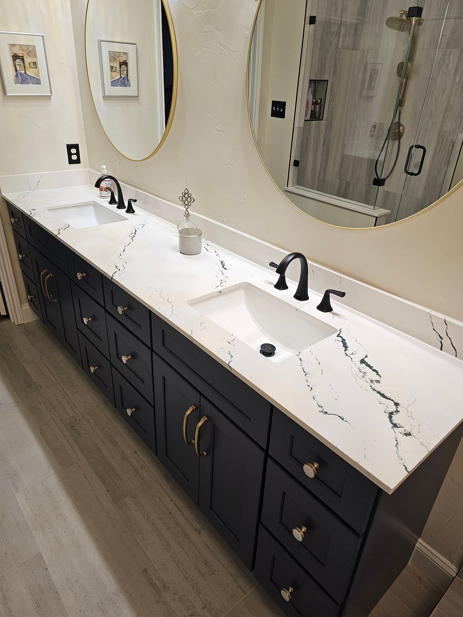 Bathroom with dark blue double vanity, white countertop, gold framed mirrors, and black fixtures.