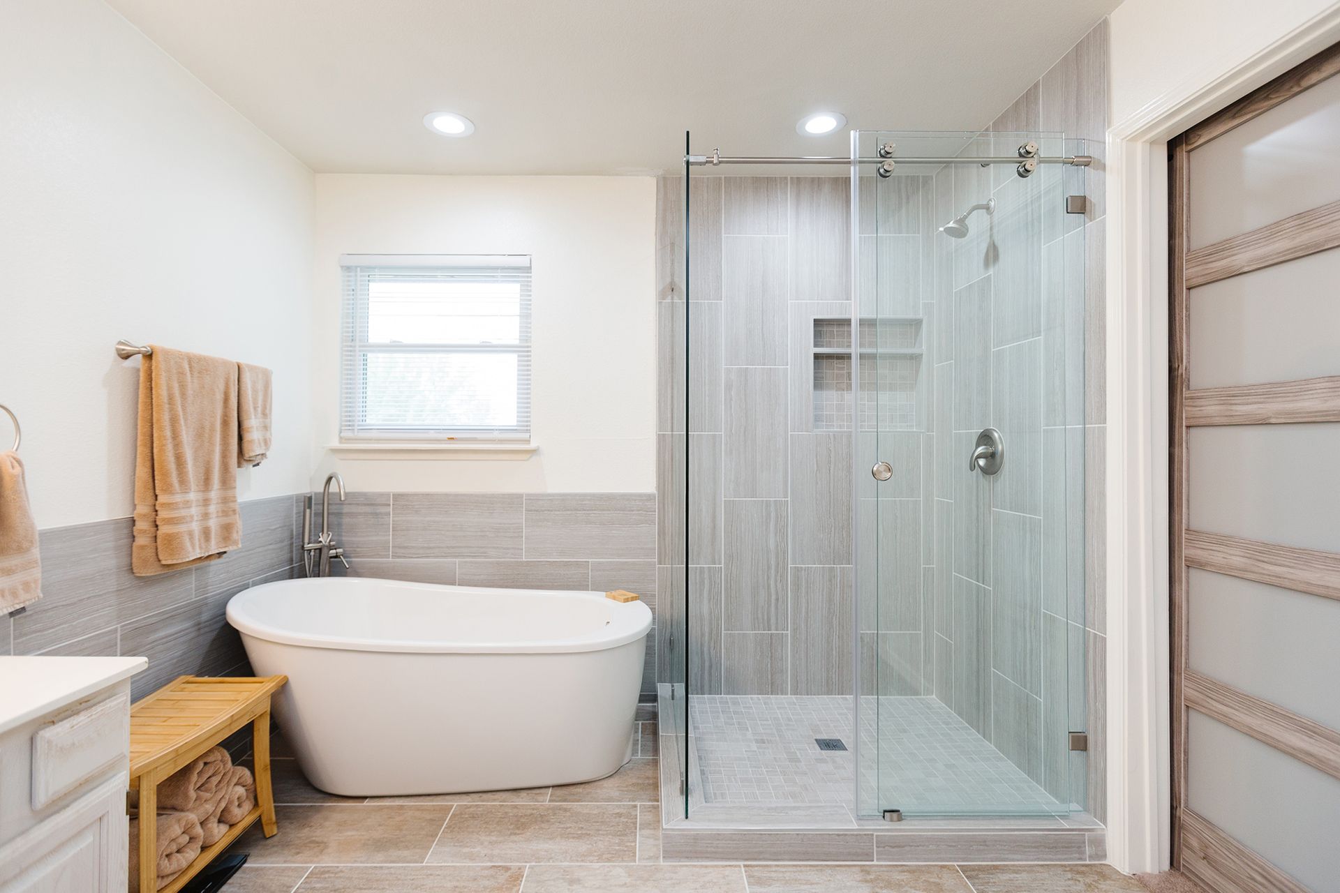 Spacious modern bathroom with a freestanding tub, walk-in shower, light gray tile, and a sliding glass door.