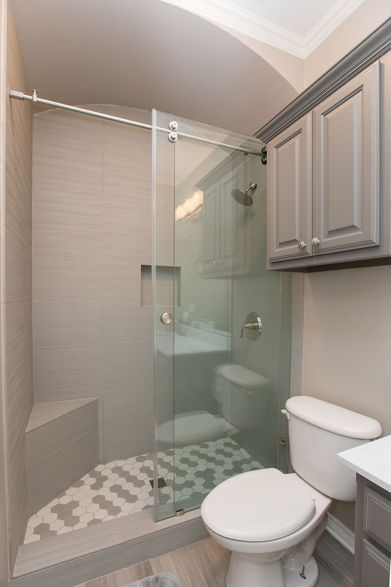 Shower stall with sliding glass door, toilet, and cabinet in a small bathroom.