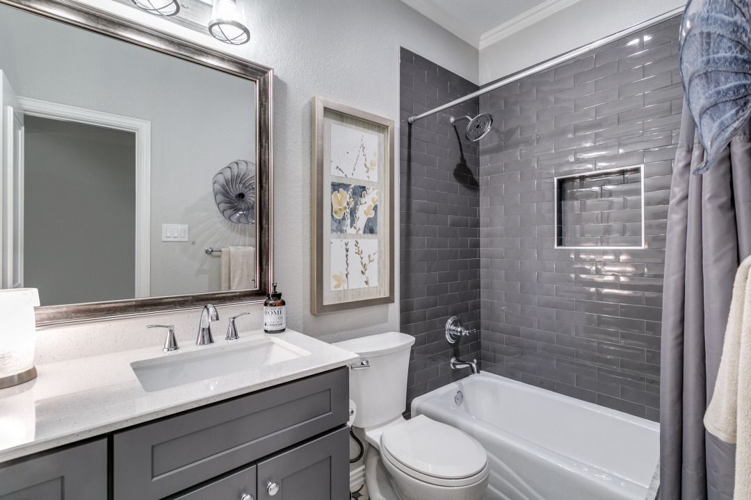 Gray bathroom with a tub, toilet, sink, and framed art.
