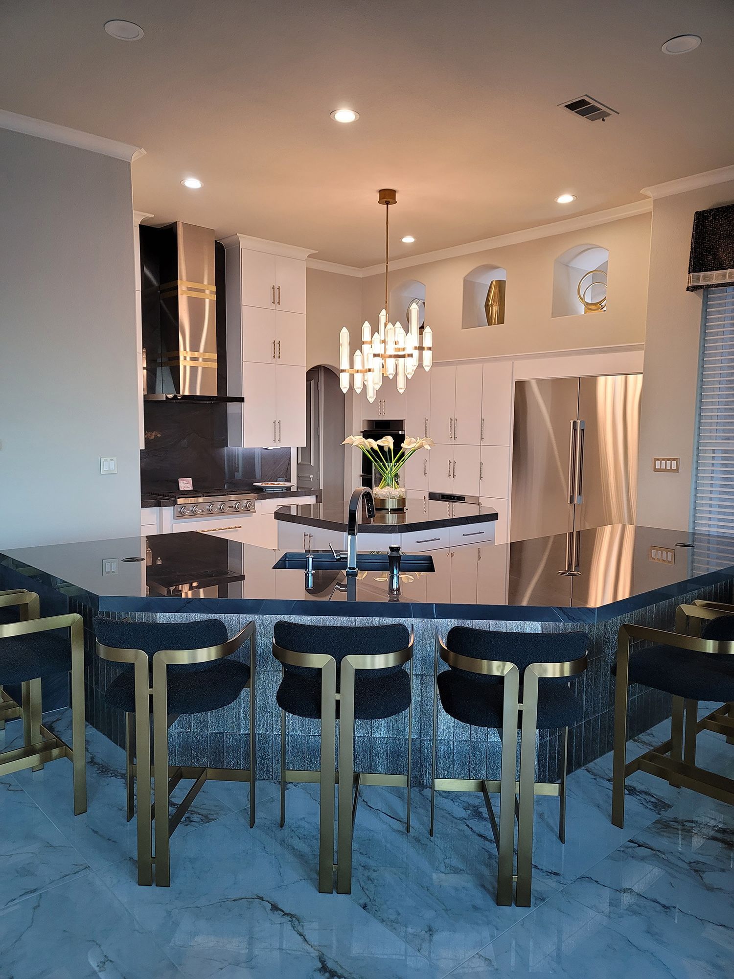 Modern kitchen with island seating; black and gold bar stools, granite countertop, white cabinets, chandelier.