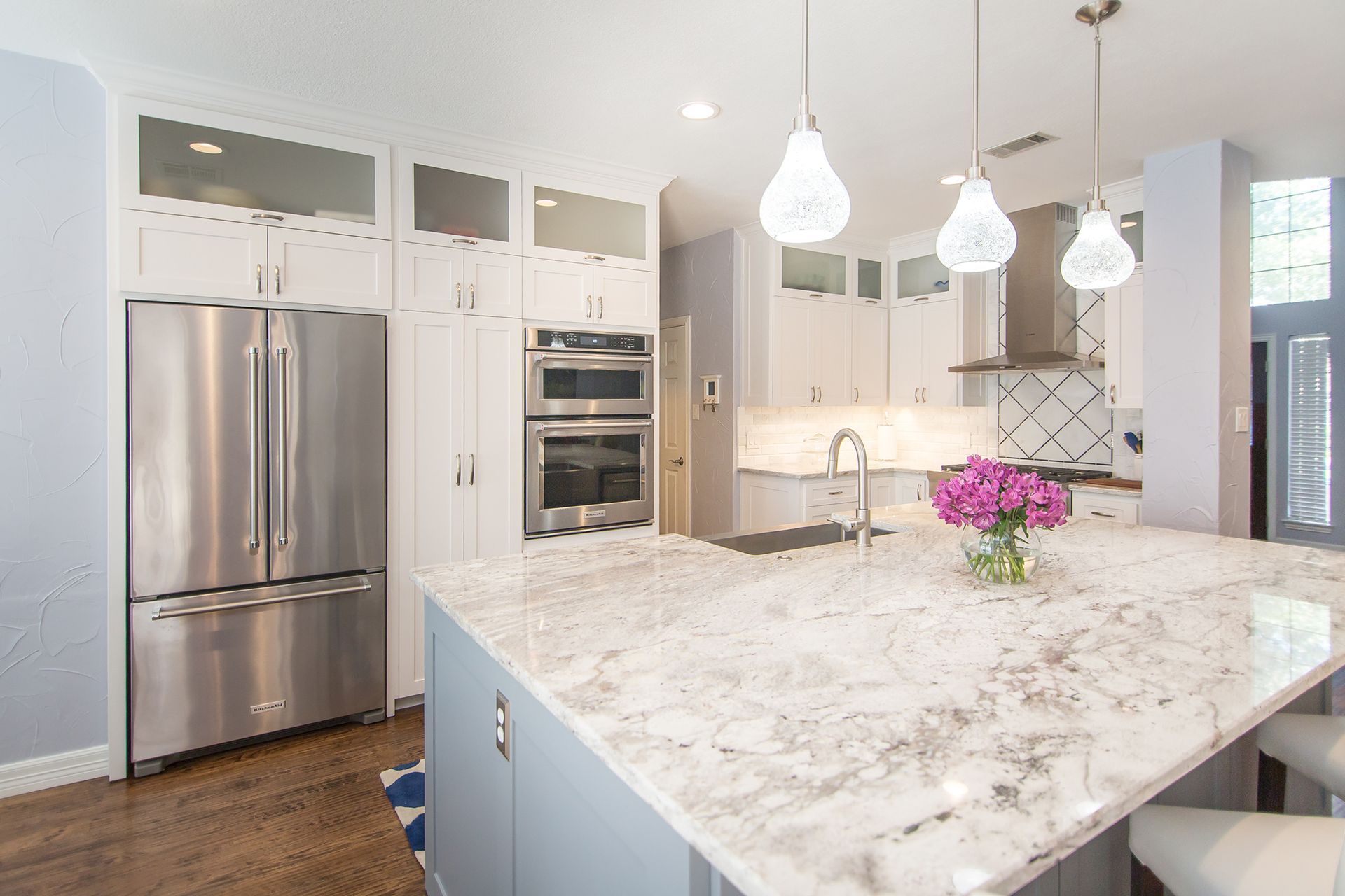 Modern kitchen with stainless steel appliances, light gray cabinets, granite island, and pendant lights.