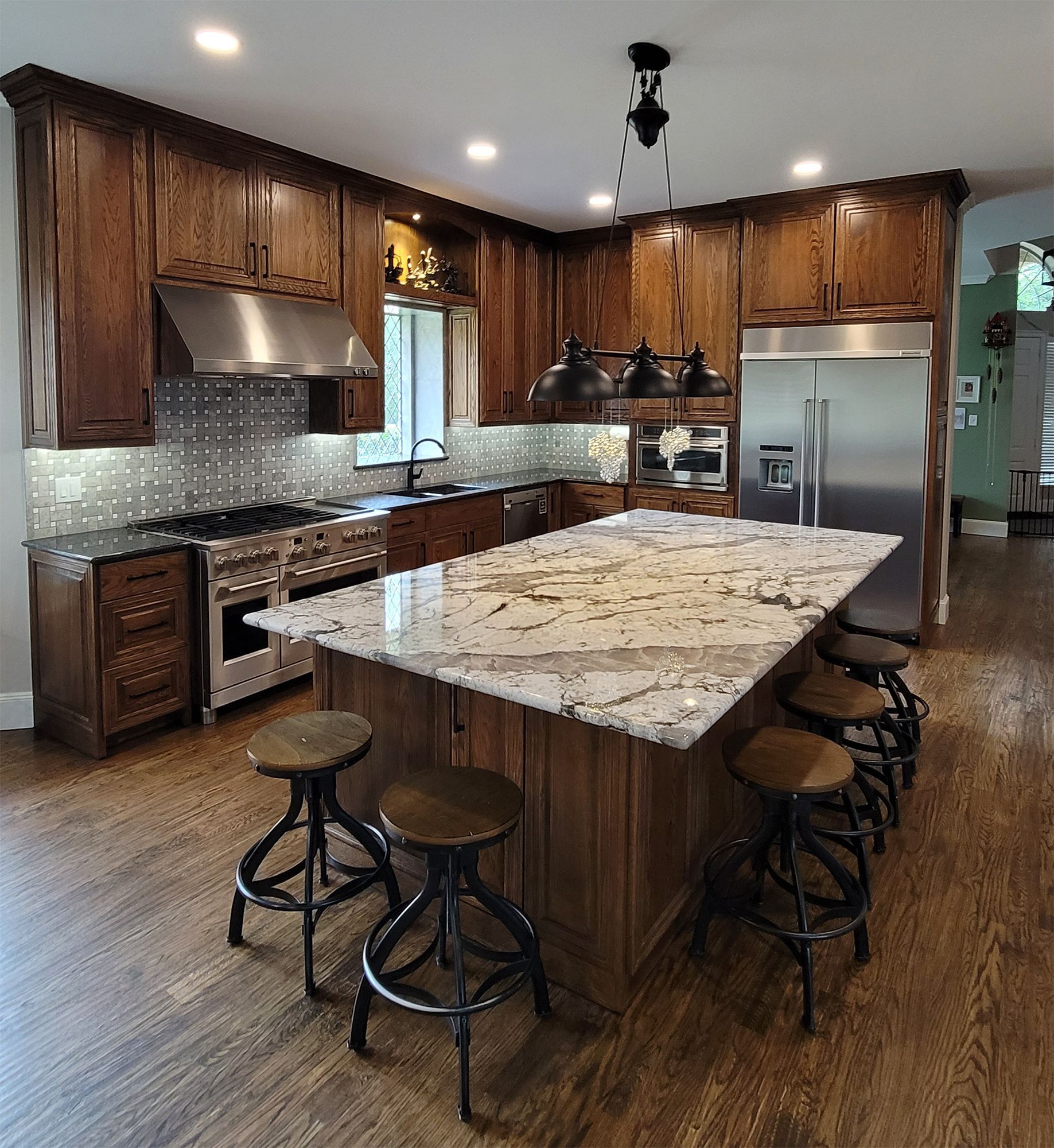Spacious kitchen with wooden cabinets, large island with granite countertop, and industrial-style bar stools.