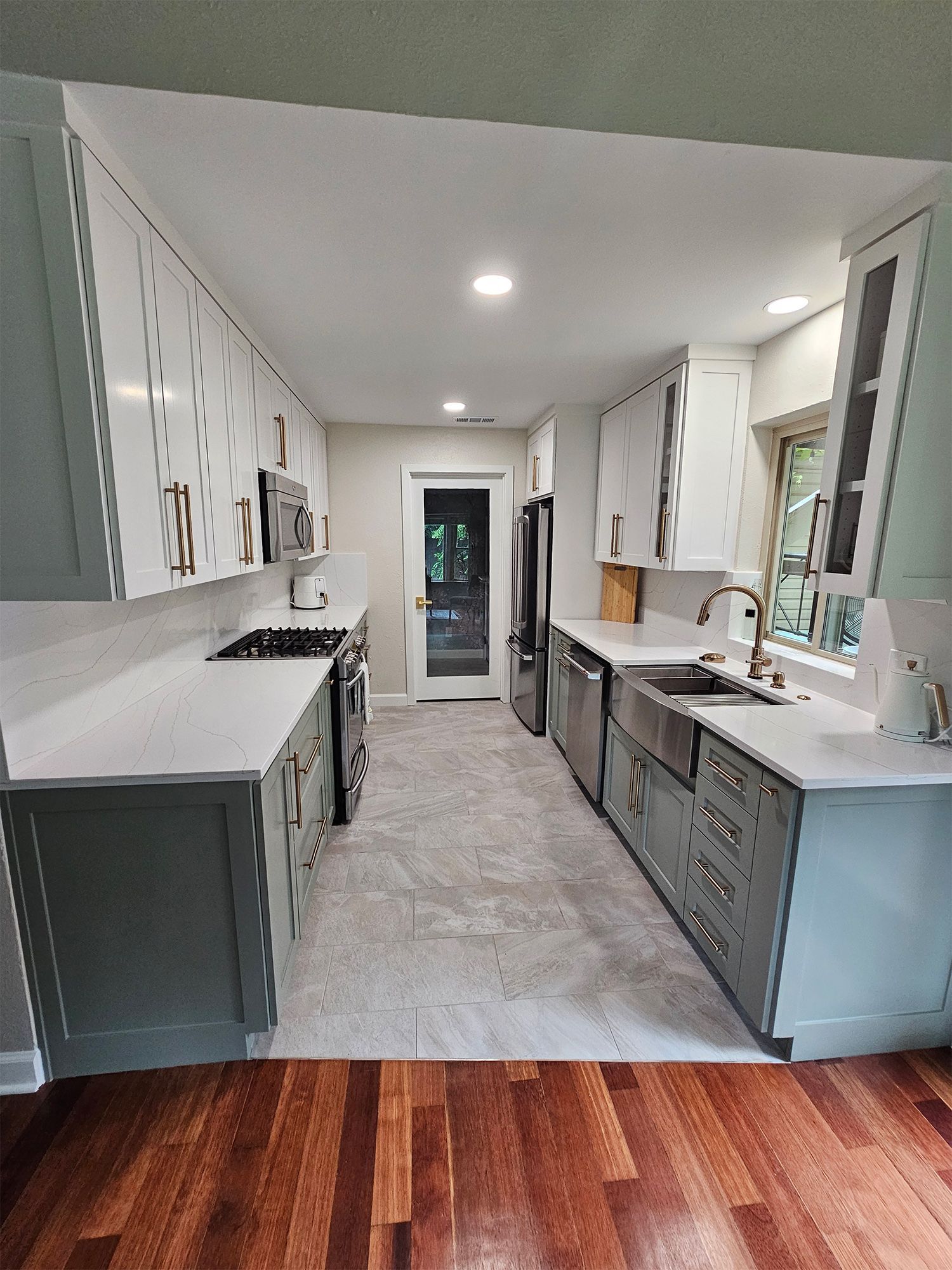 Modern kitchen with white and green cabinets, stainless steel appliances, and wood floor.