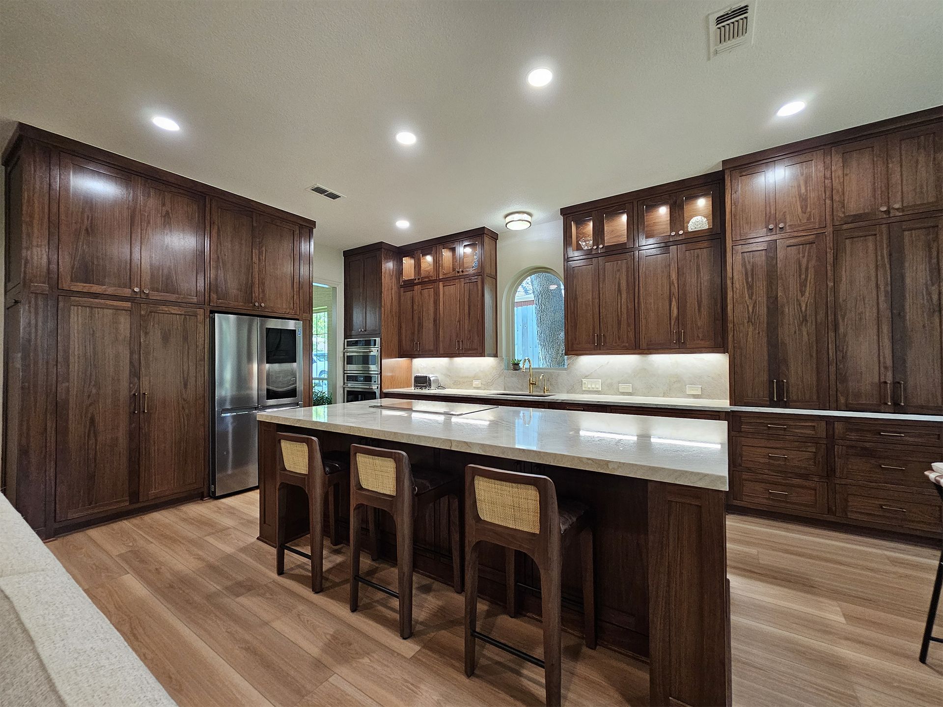 Spacious kitchen with dark wood cabinets, island with stools, light countertops, and stainless steel appliances.