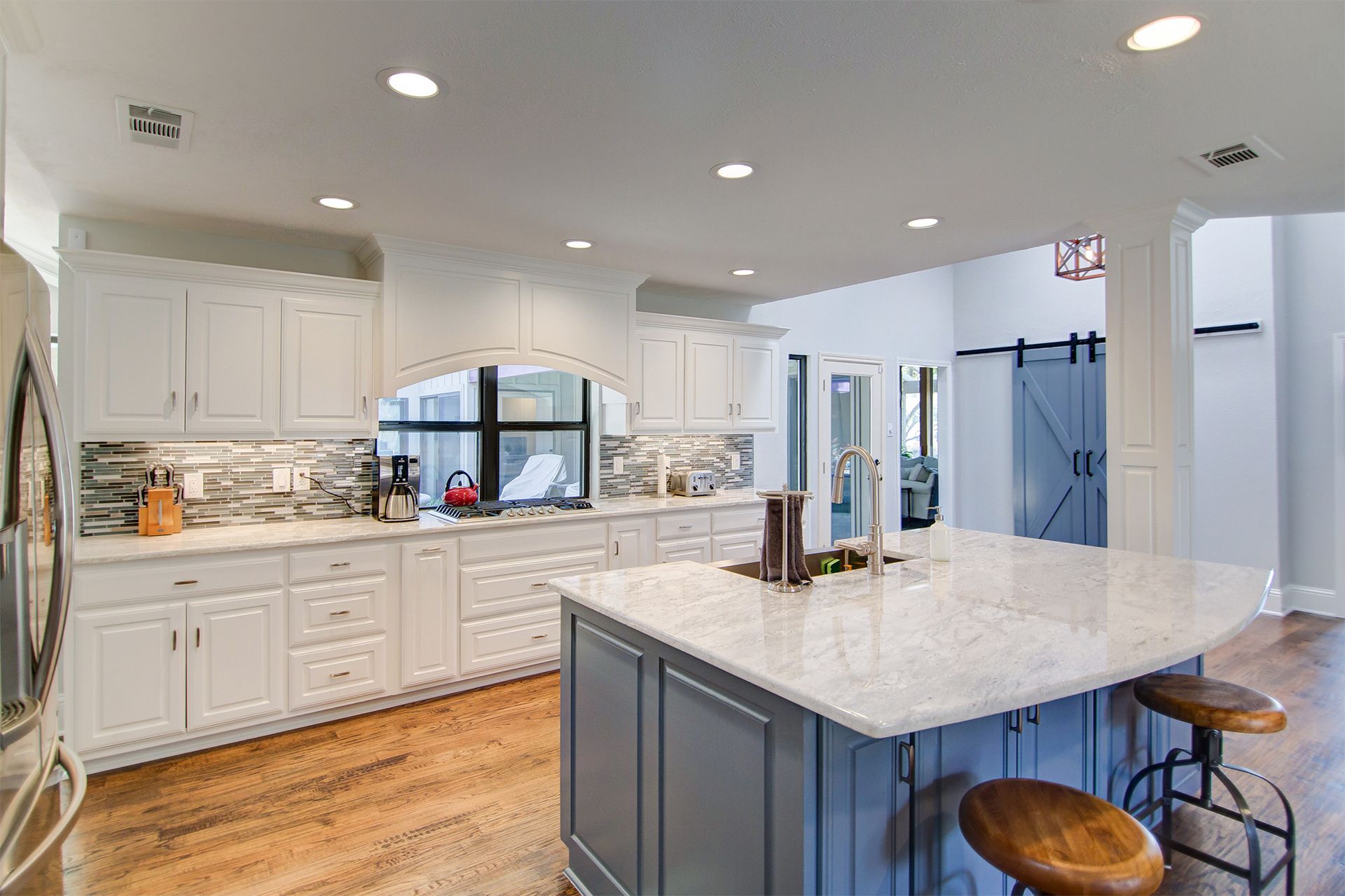 Bright white kitchen with a blue island, granite countertops, and wooden floors.