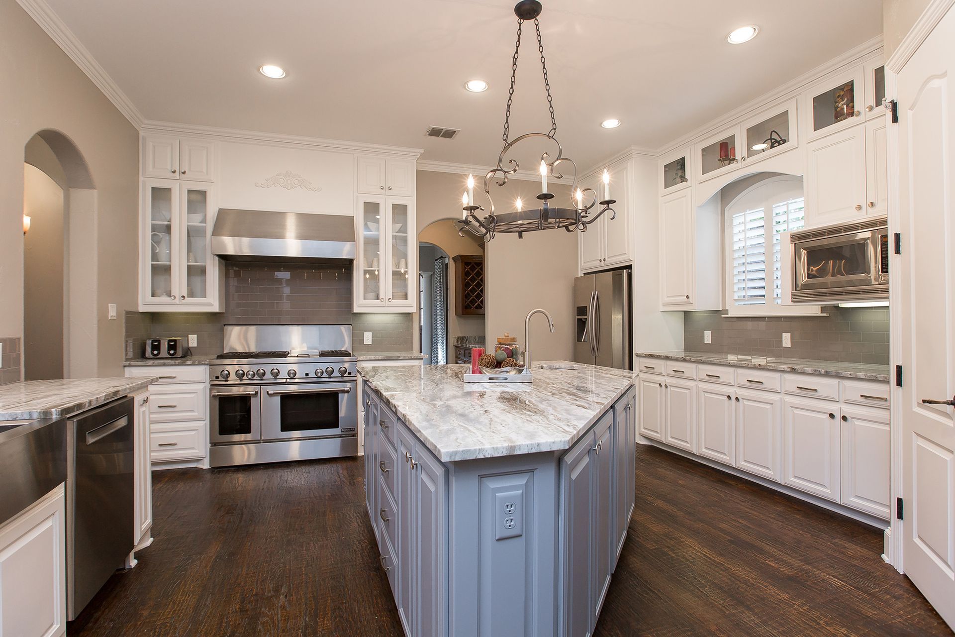Upscale kitchen with white cabinets, gray island, stainless steel appliances, and dark wood floors.