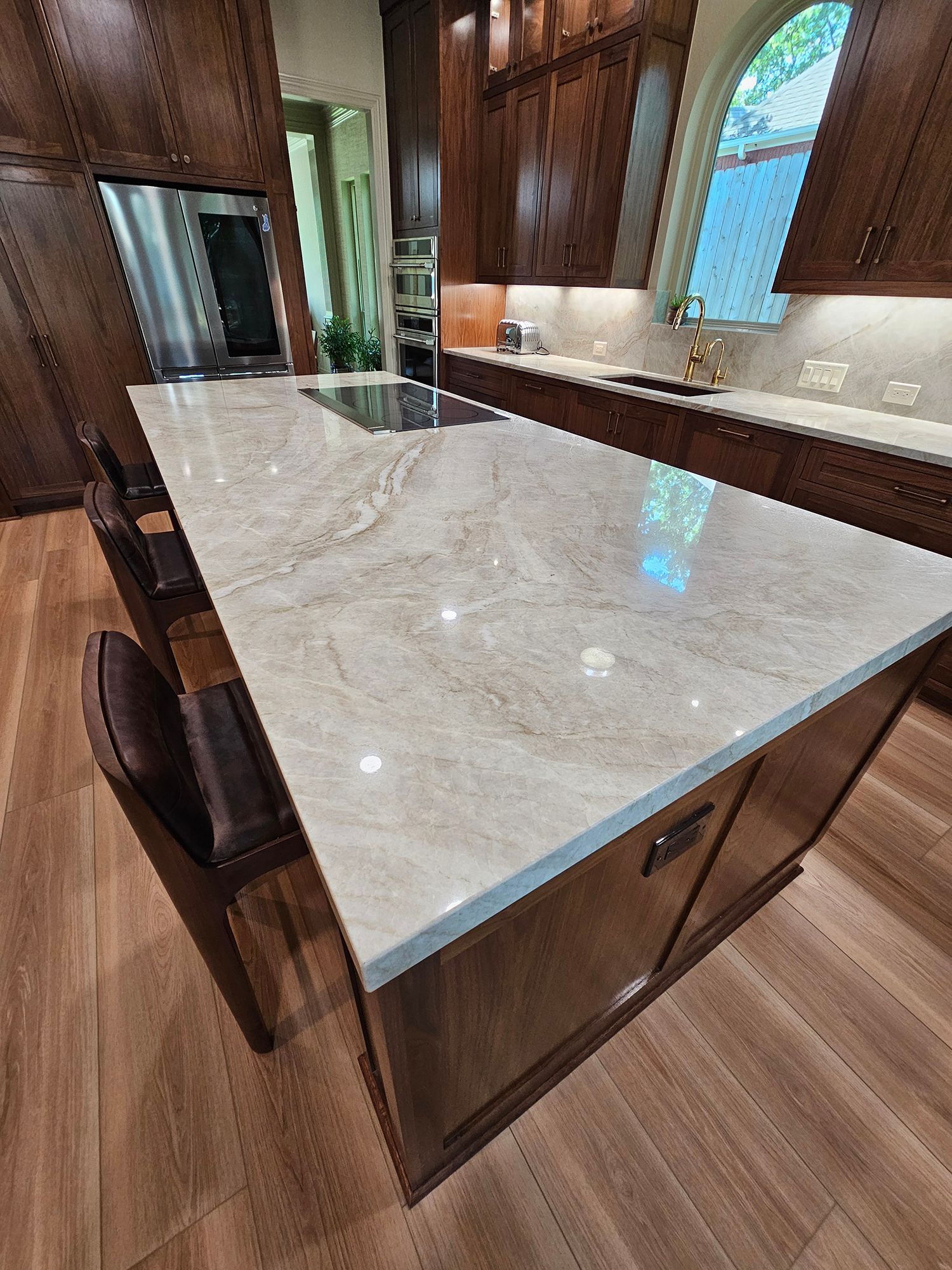 Kitchen island with a stone countertop and seating; wood cabinets and flooring.
