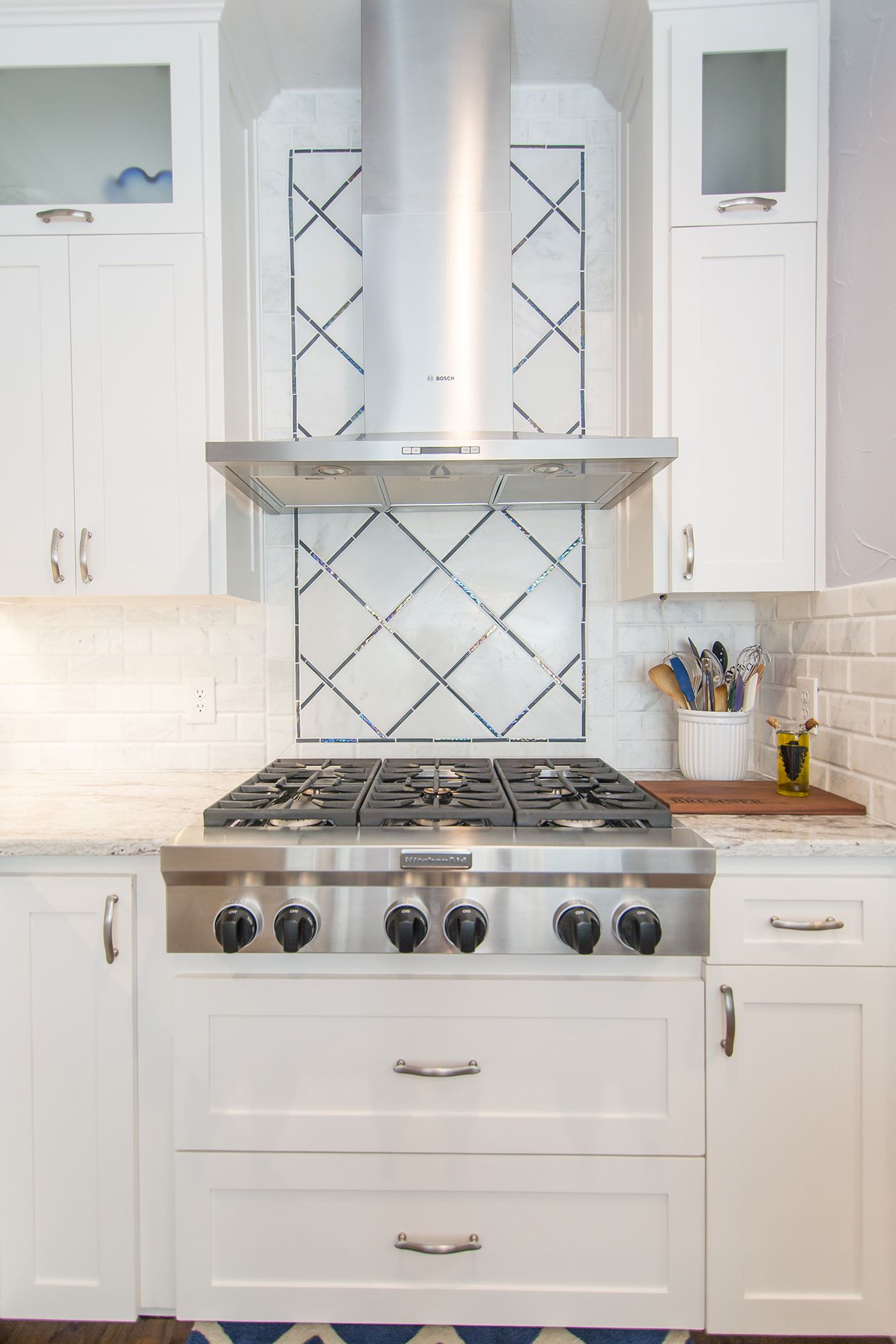 White kitchen with stainless steel range, hood, and diamond patterned backsplash.
