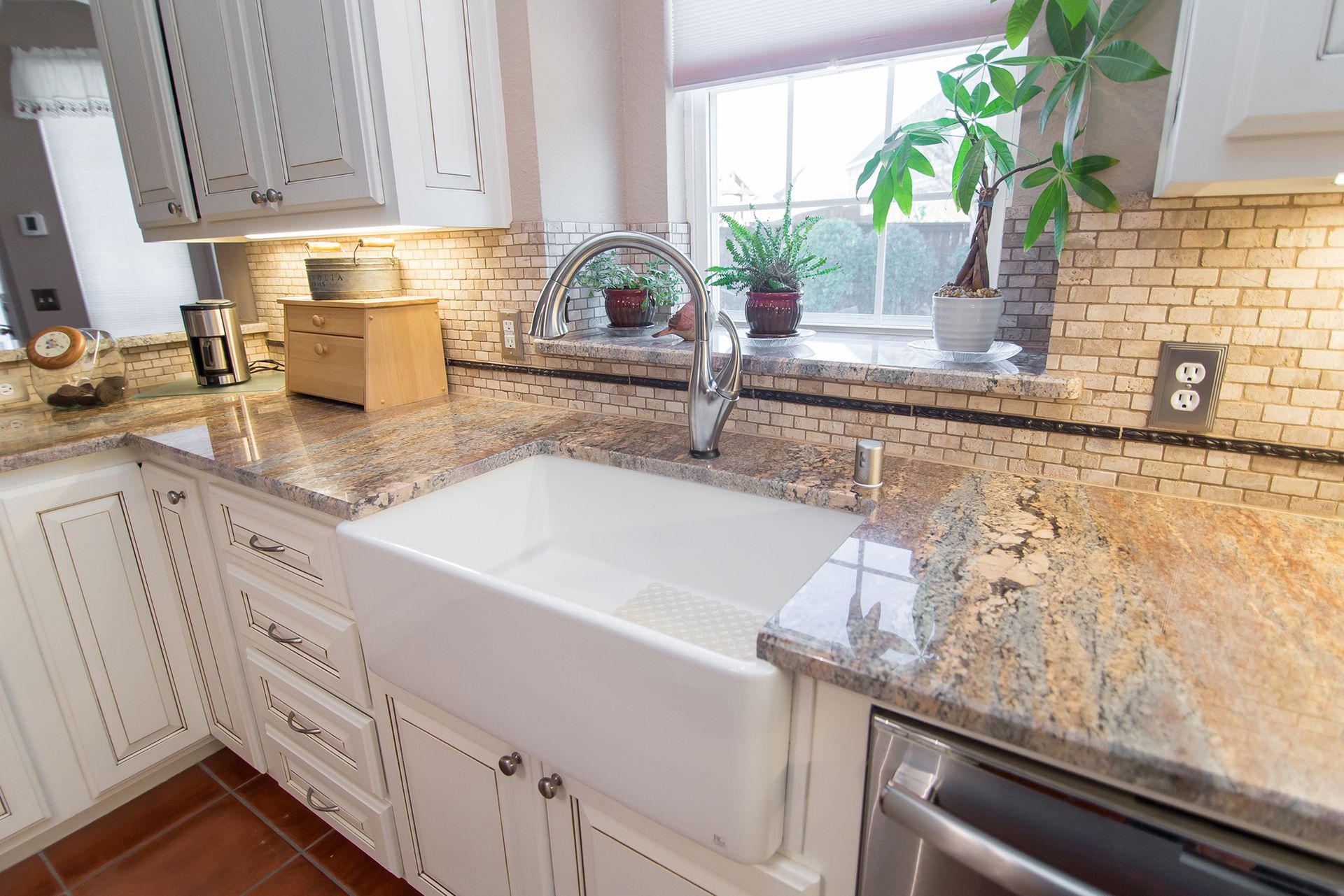 White farmhouse sink in a kitchen with granite countertops and tile backsplash.
