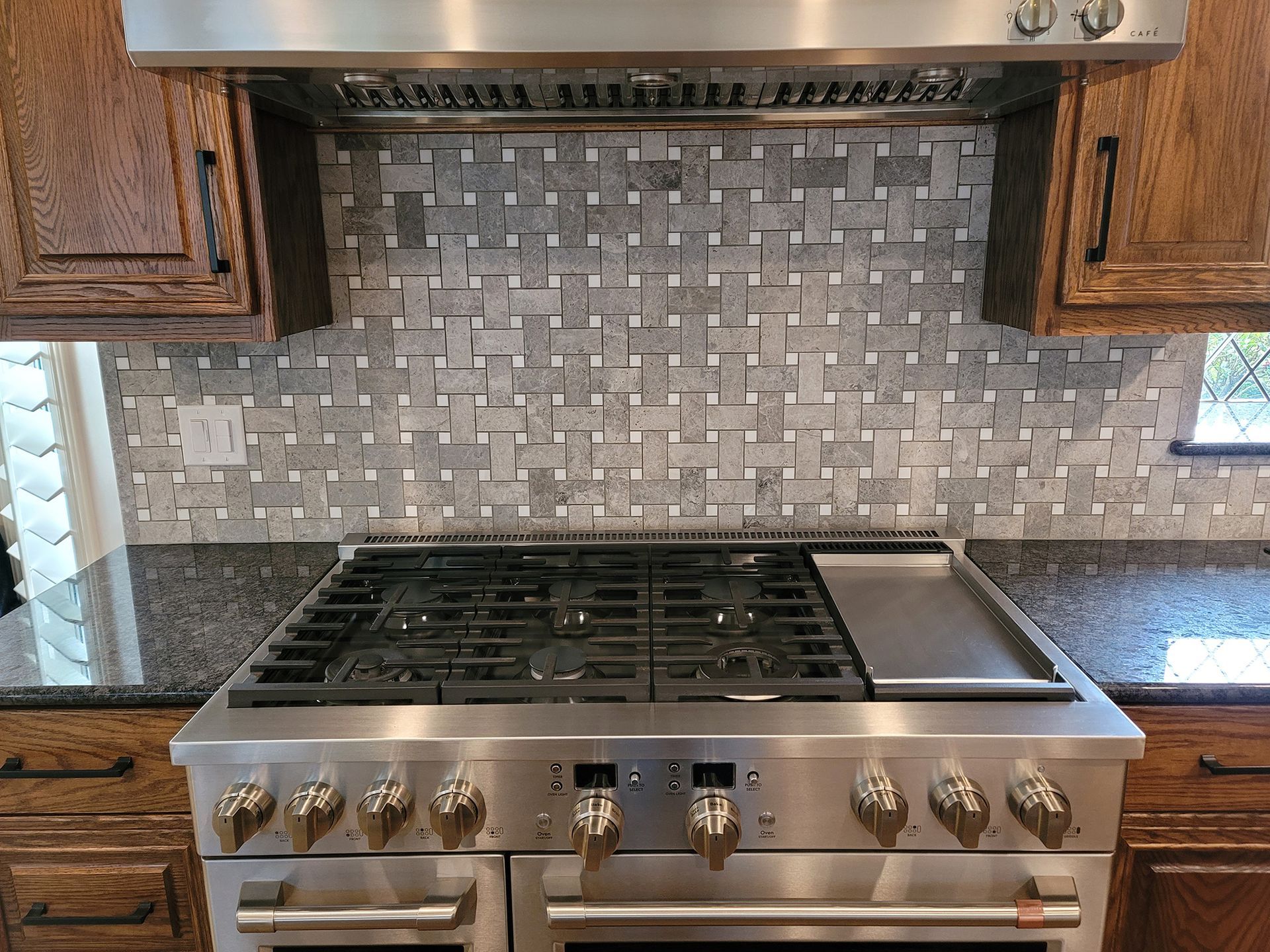 Stainless steel range with dark cabinets and gray tile backsplash in a kitchen.
