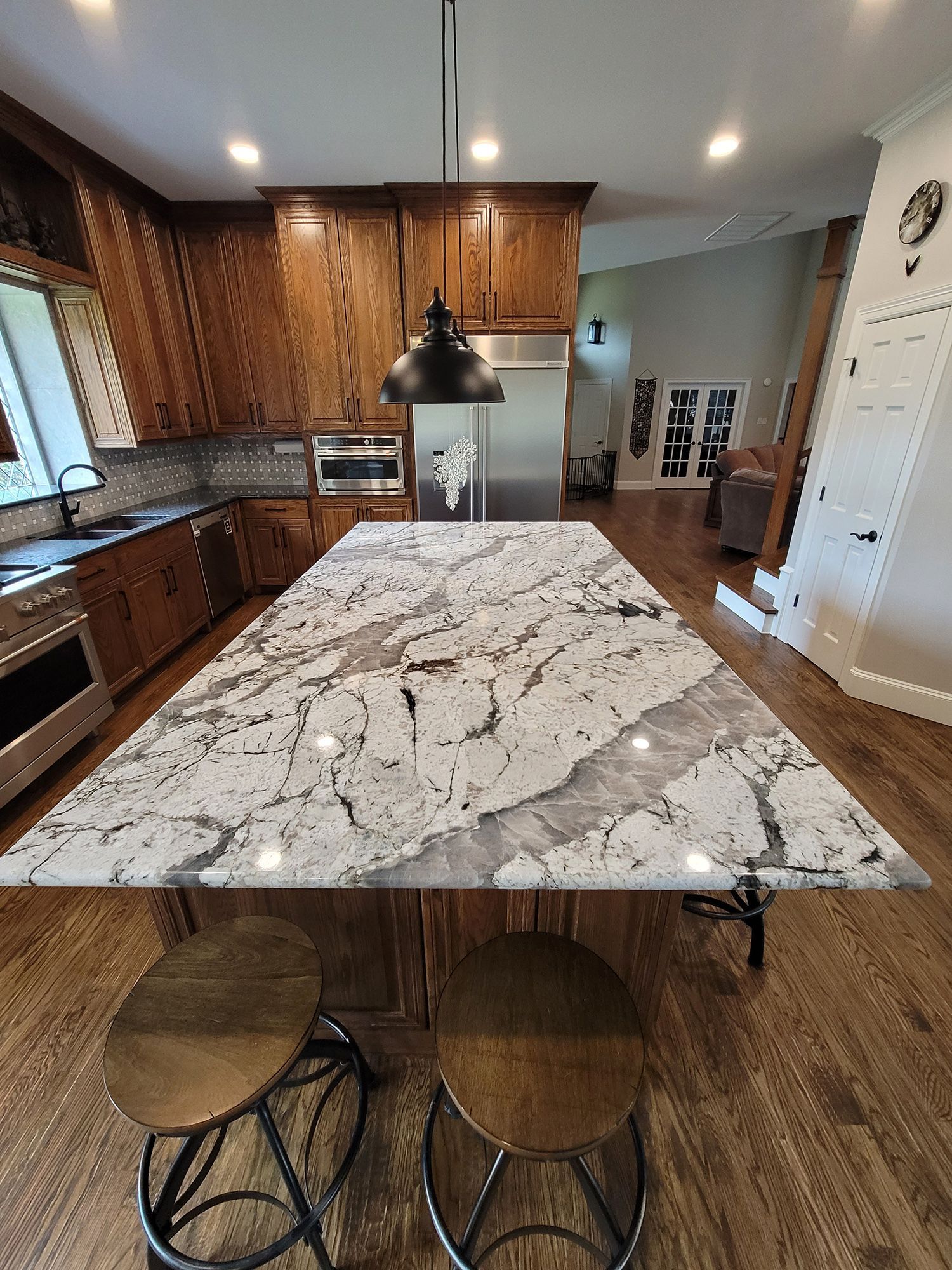 Spacious kitchen with a large granite island and wooden cabinets. Two stools sit at the island.