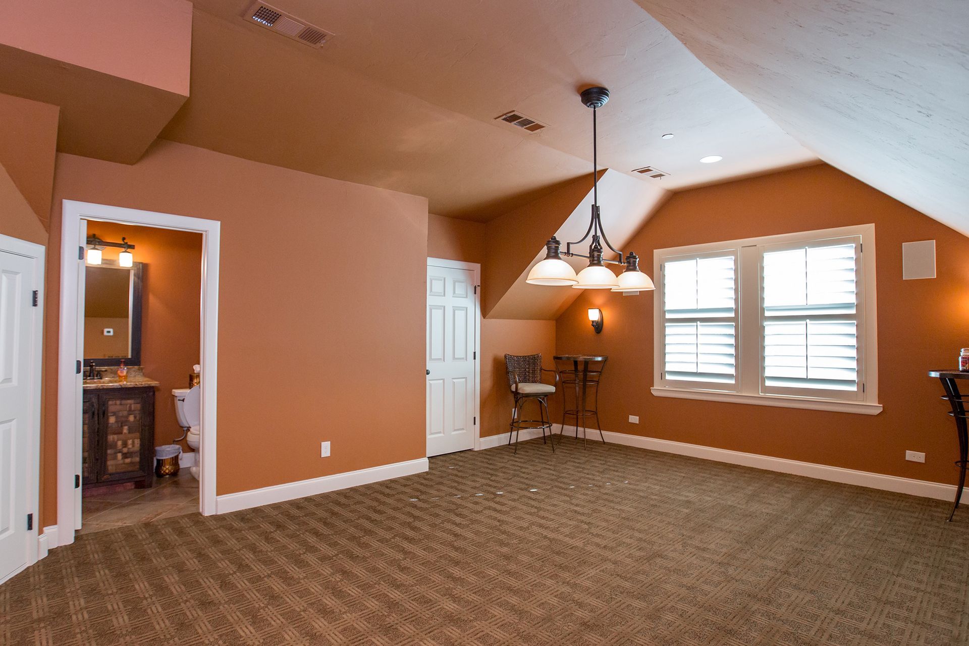 Interior of a room with orange walls, carpet, a small table, and a window. A door to the bathroom is visible.