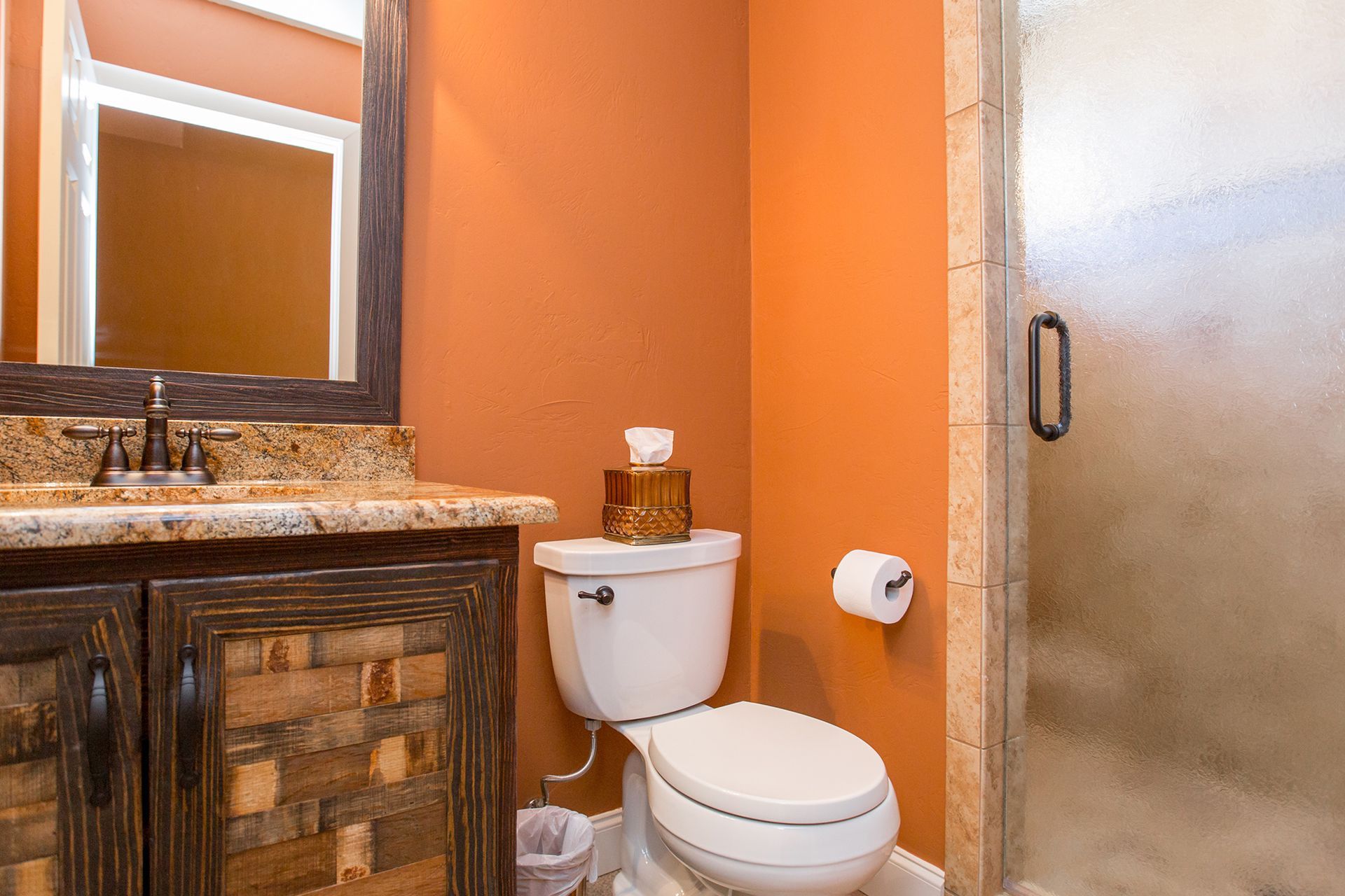 Bathroom with orange walls, a toilet, vanity, and a glass shower door.